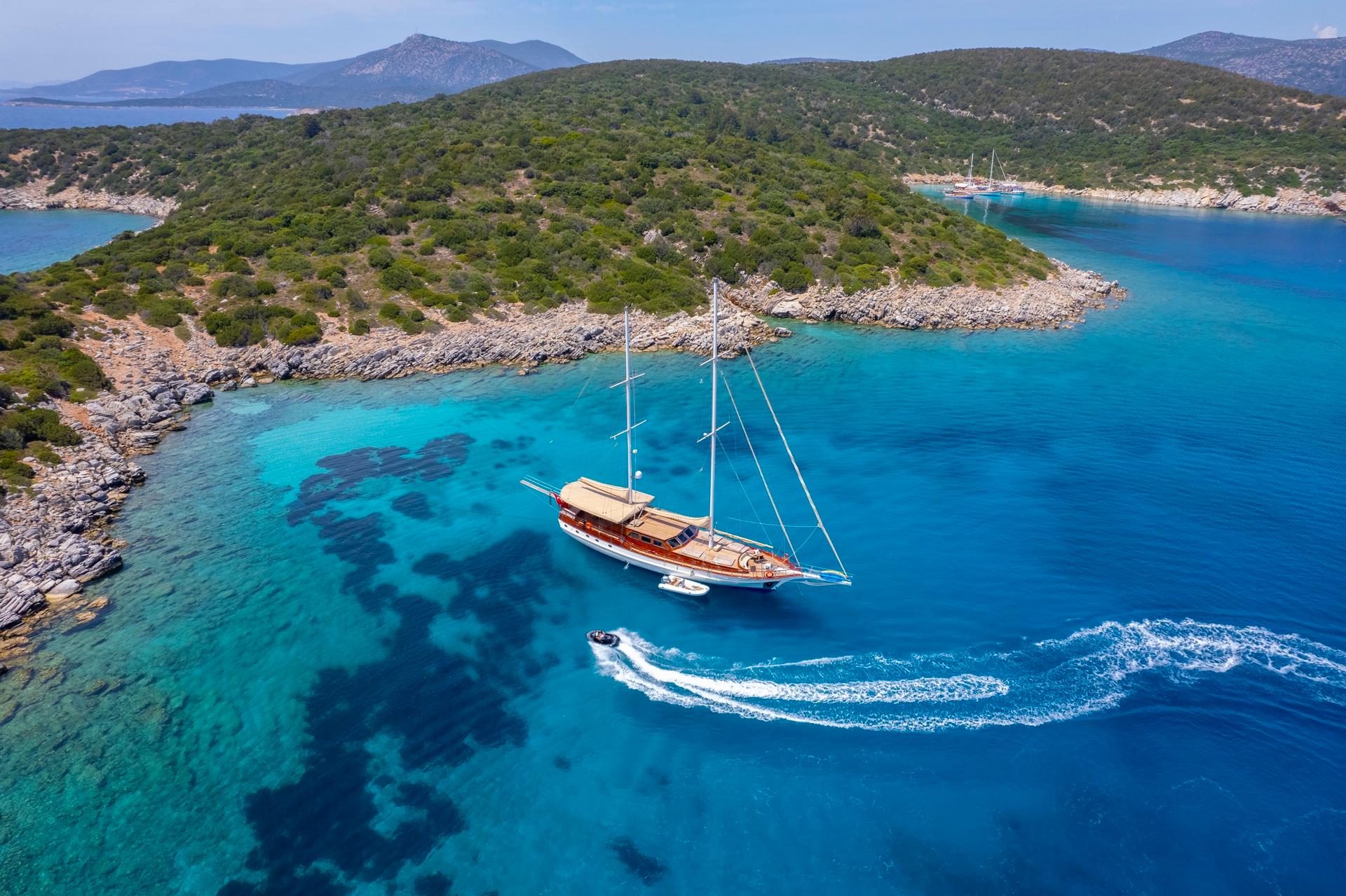 aerial view of traditional wooden gulet yacht anchored in pristine turquoise bay with tender boat