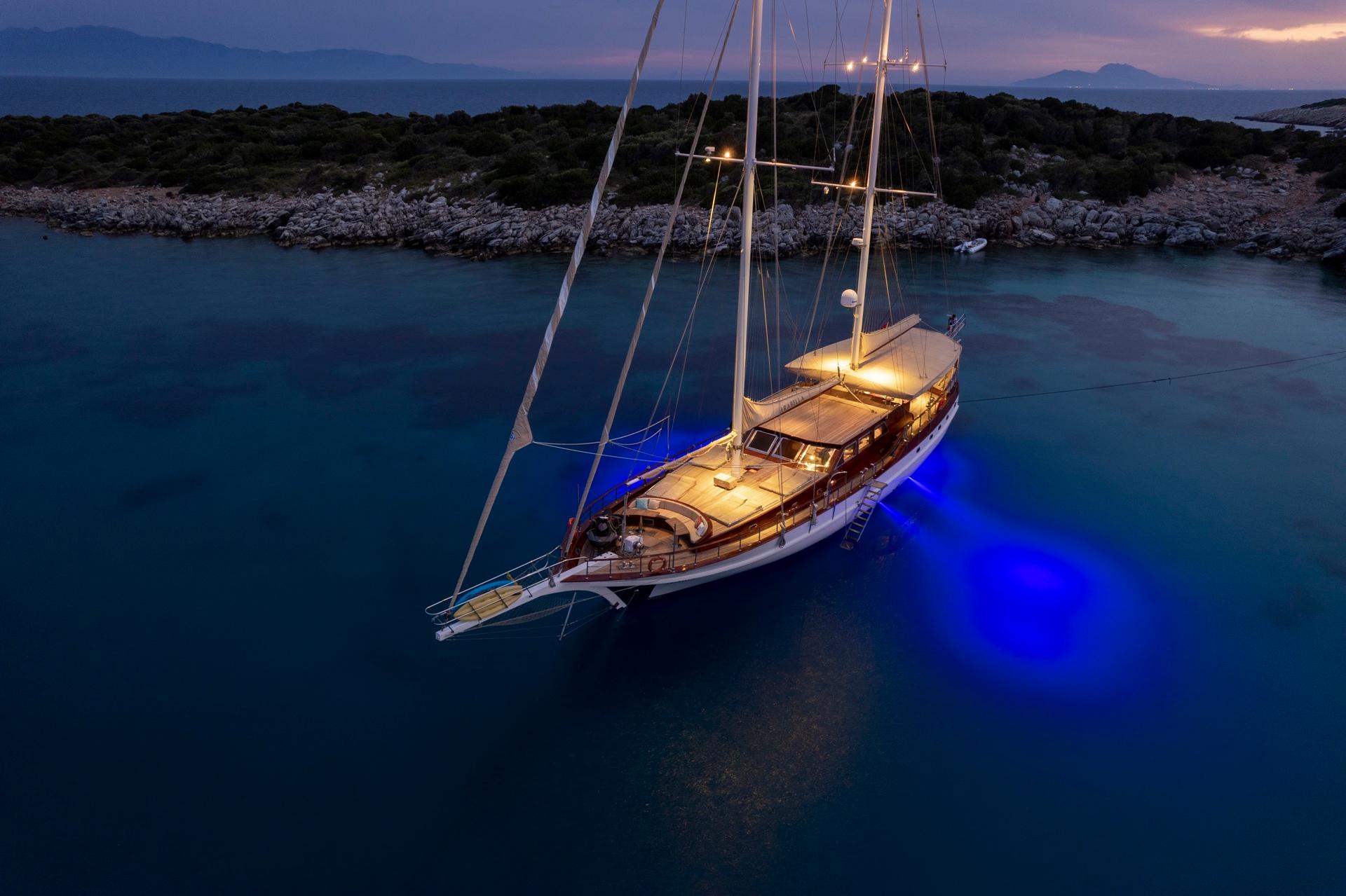 aerial view of traditional wooden gulet yacht anchored in secluded bay with blue underwater lighting at twilight