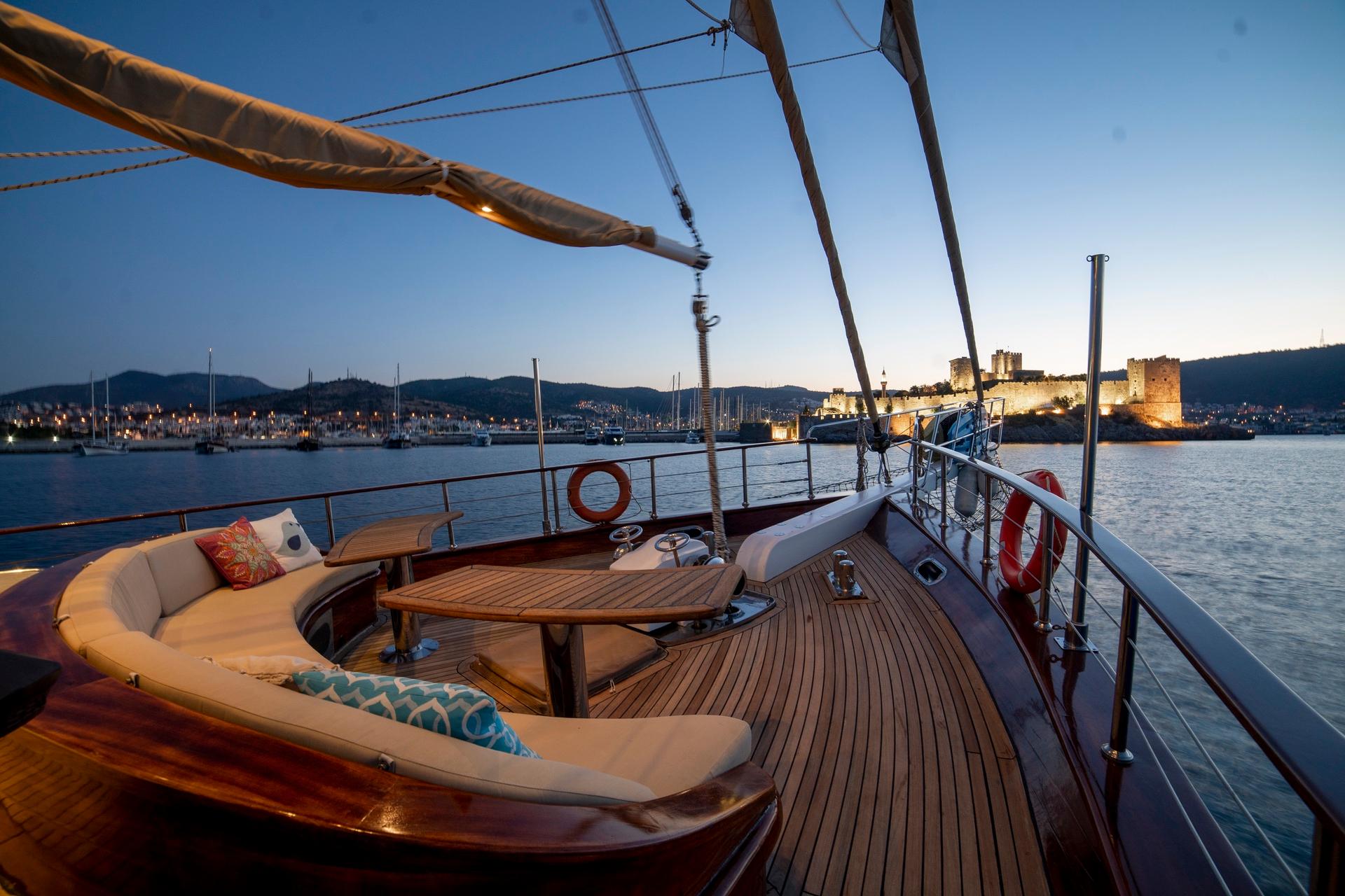 yacht aft deck with curved white seating, teak decking and medieval castle harbor view at dusk