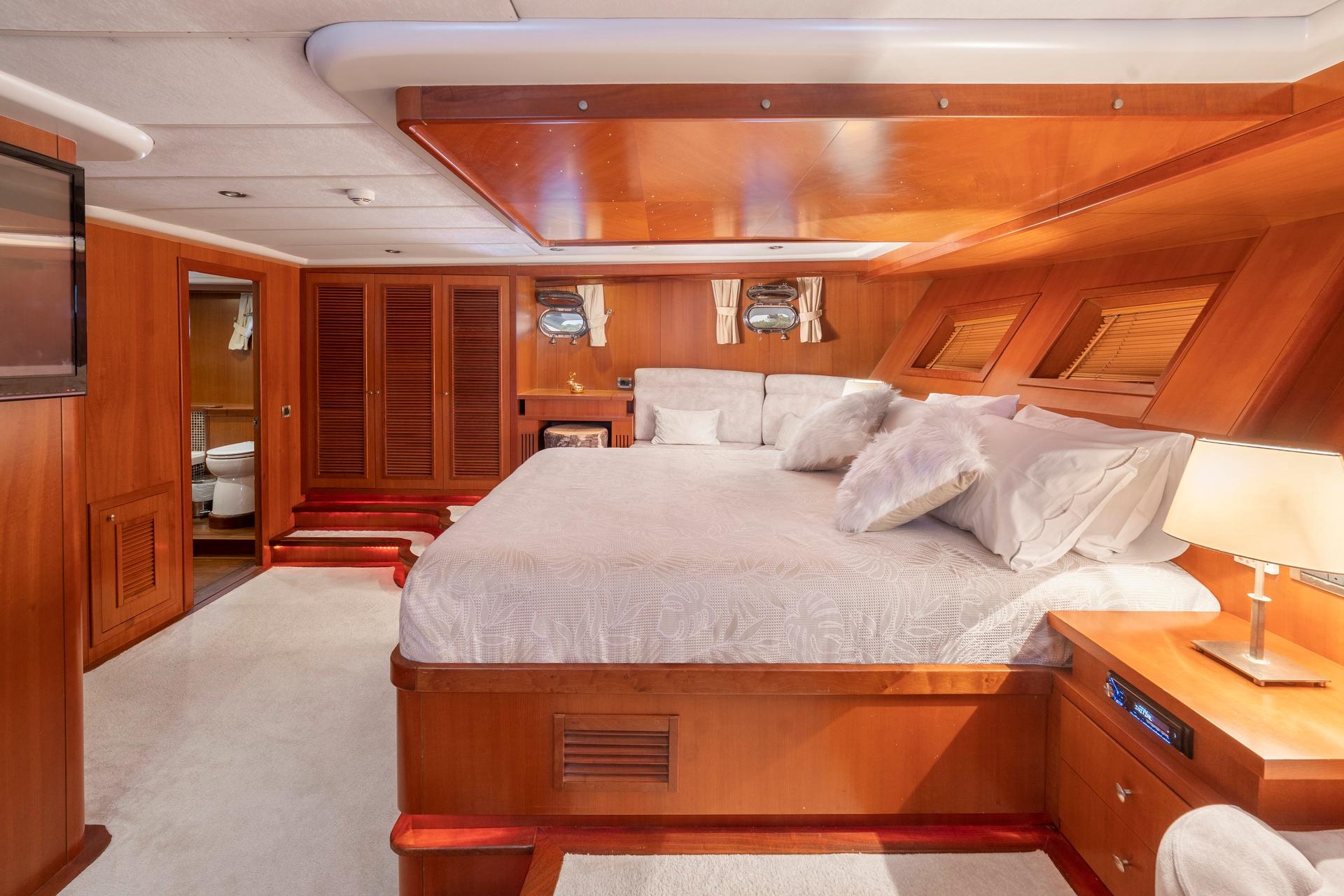 luxury yacht master cabin with king bed, wooden paneling and en-suite bathroom door