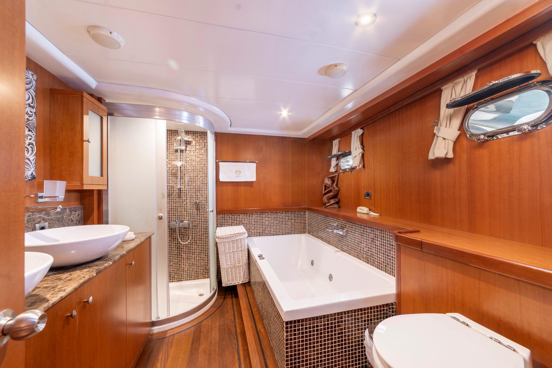 yacht master bathroom featuring built-in jacuzzi tub, marble vanity, curved shower, and warm wood paneling