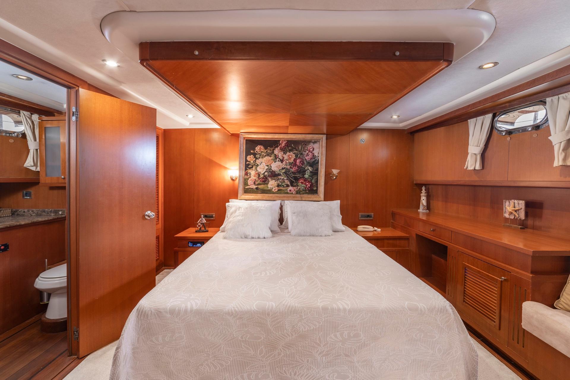 yacht cabin interior with white bedding, wood paneling, floral artwork and en-suite toilet visible