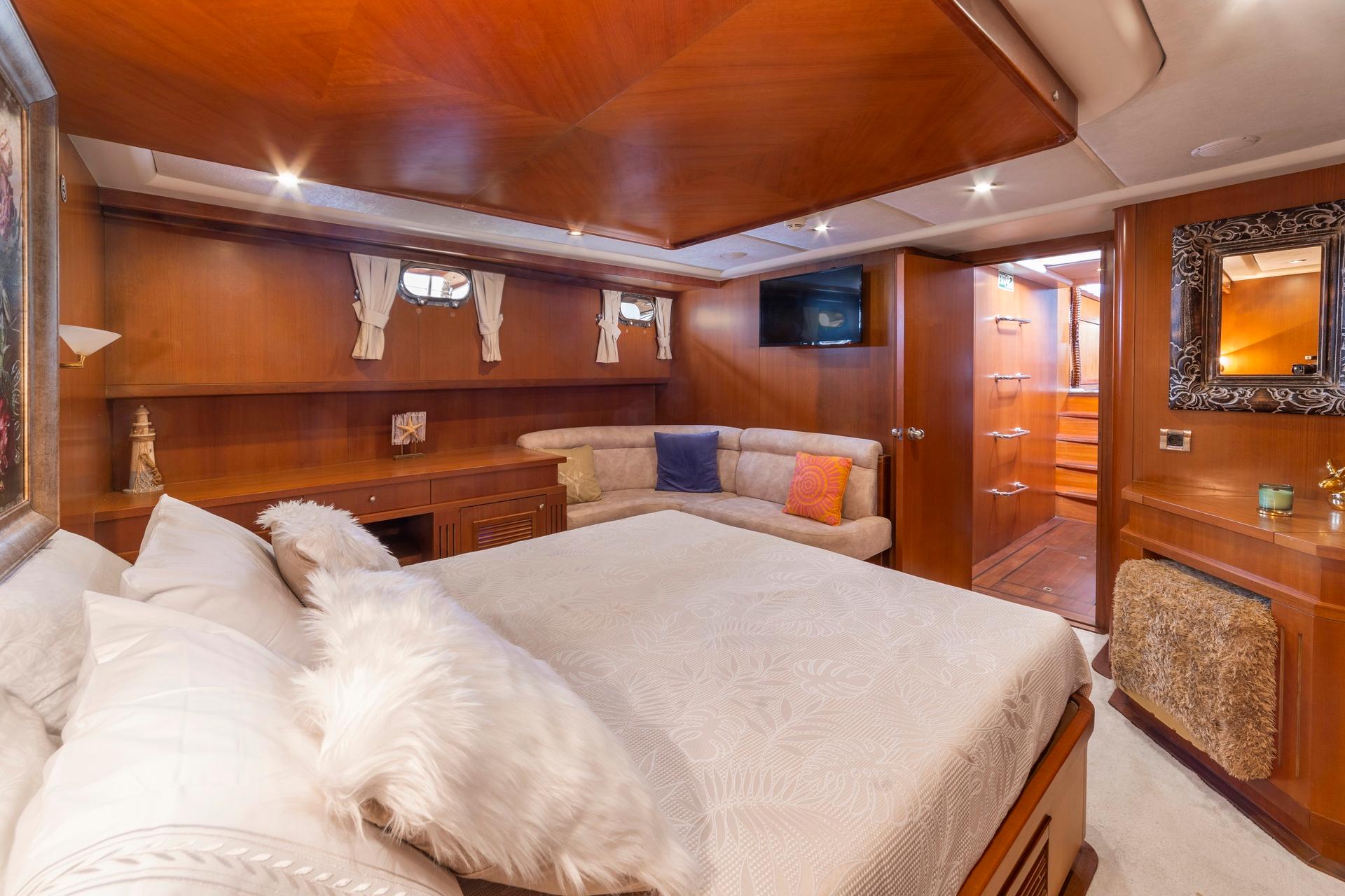 luxury yacht master cabin with king bed, built-in seating area, wooden paneling and en-suite access