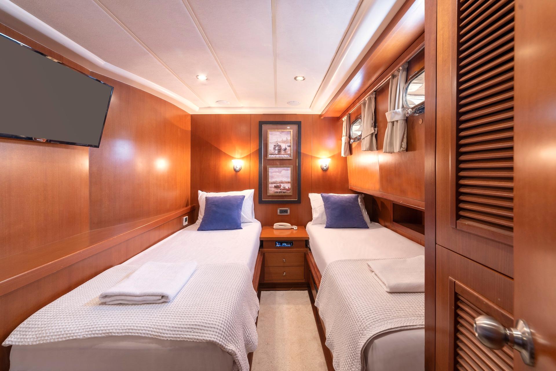 yacht twin cabin with two single beds, wood paneling, wall-mounted TV and bedside table