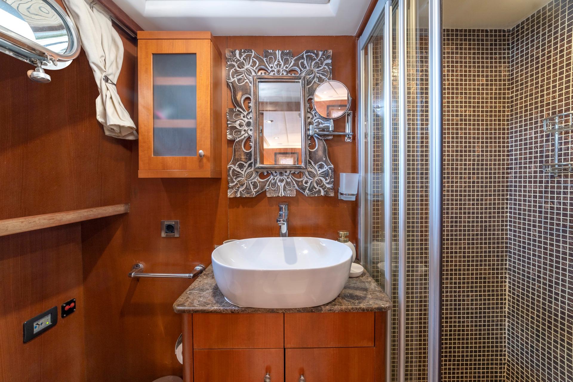 yacht bathroom featuring white oval basin, ornate mirror, and golden mosaic tile shower enclosure