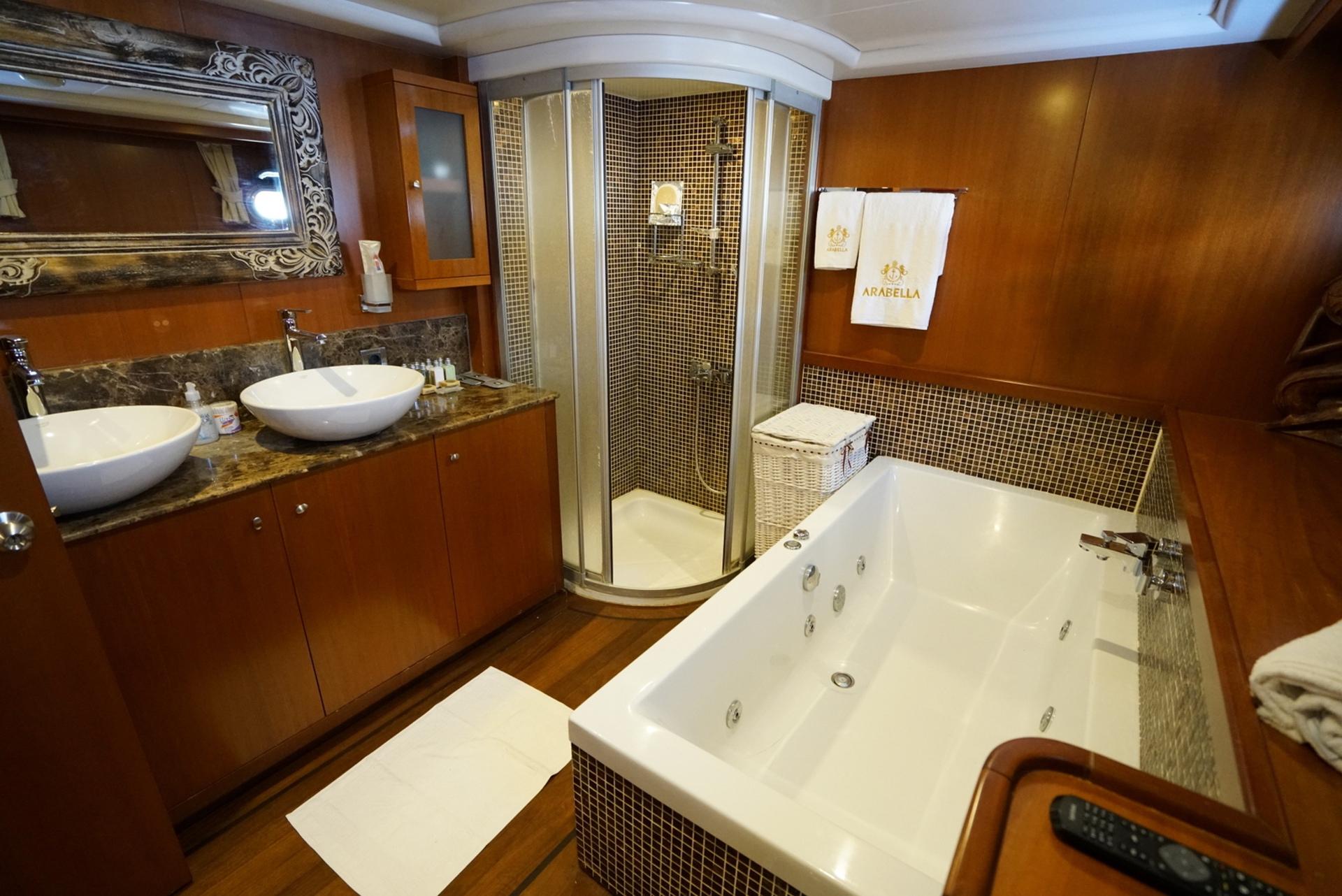 Yacht master bathroom featuring built-in jacuzzi, curved glass shower, double basin vanity with marble countertop