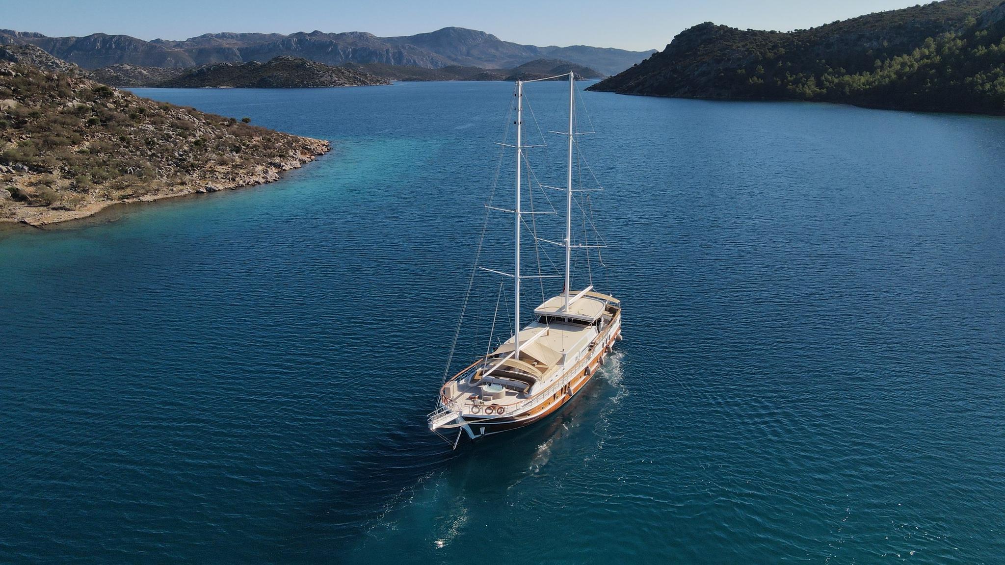 aerial view of wooden gulet yacht anchored in turquoise bay surrounded by mountainous coastline