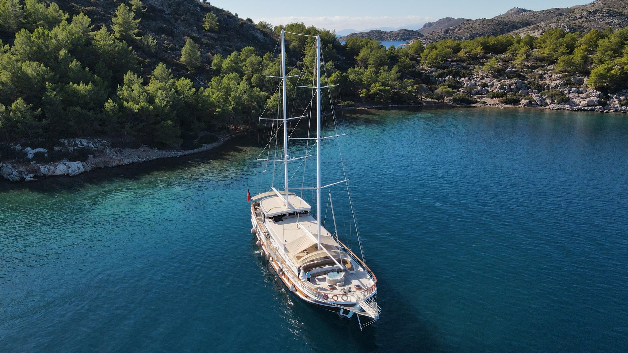 aerial view of traditional wooden gulet anchored in turquoise bay surrounded by pine forests