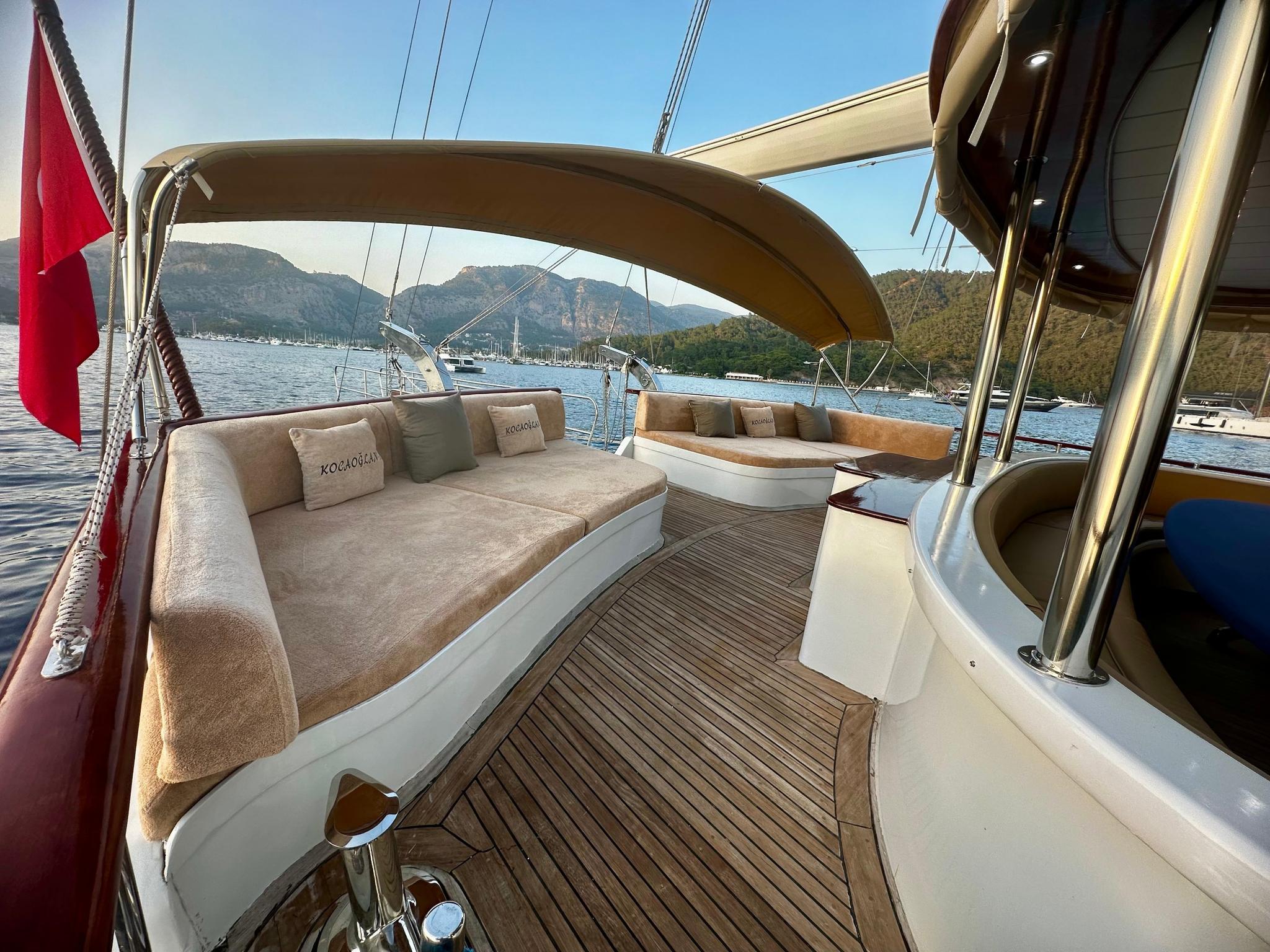 Gulet aft deck with curved cushioned seating areas and teak decking overlooking bay
