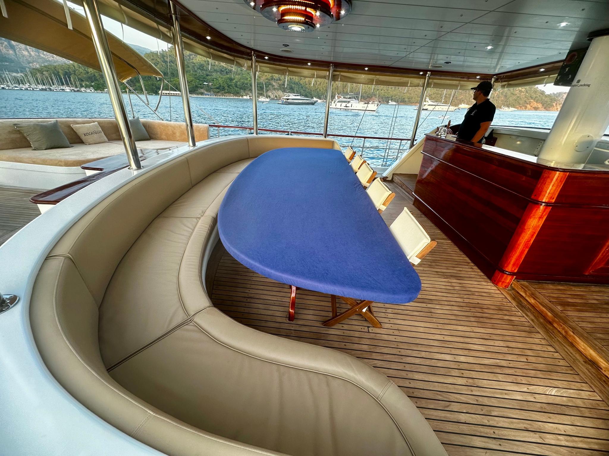yacht covered aft deck with curved cream seating, blue oval dining table and teak flooring