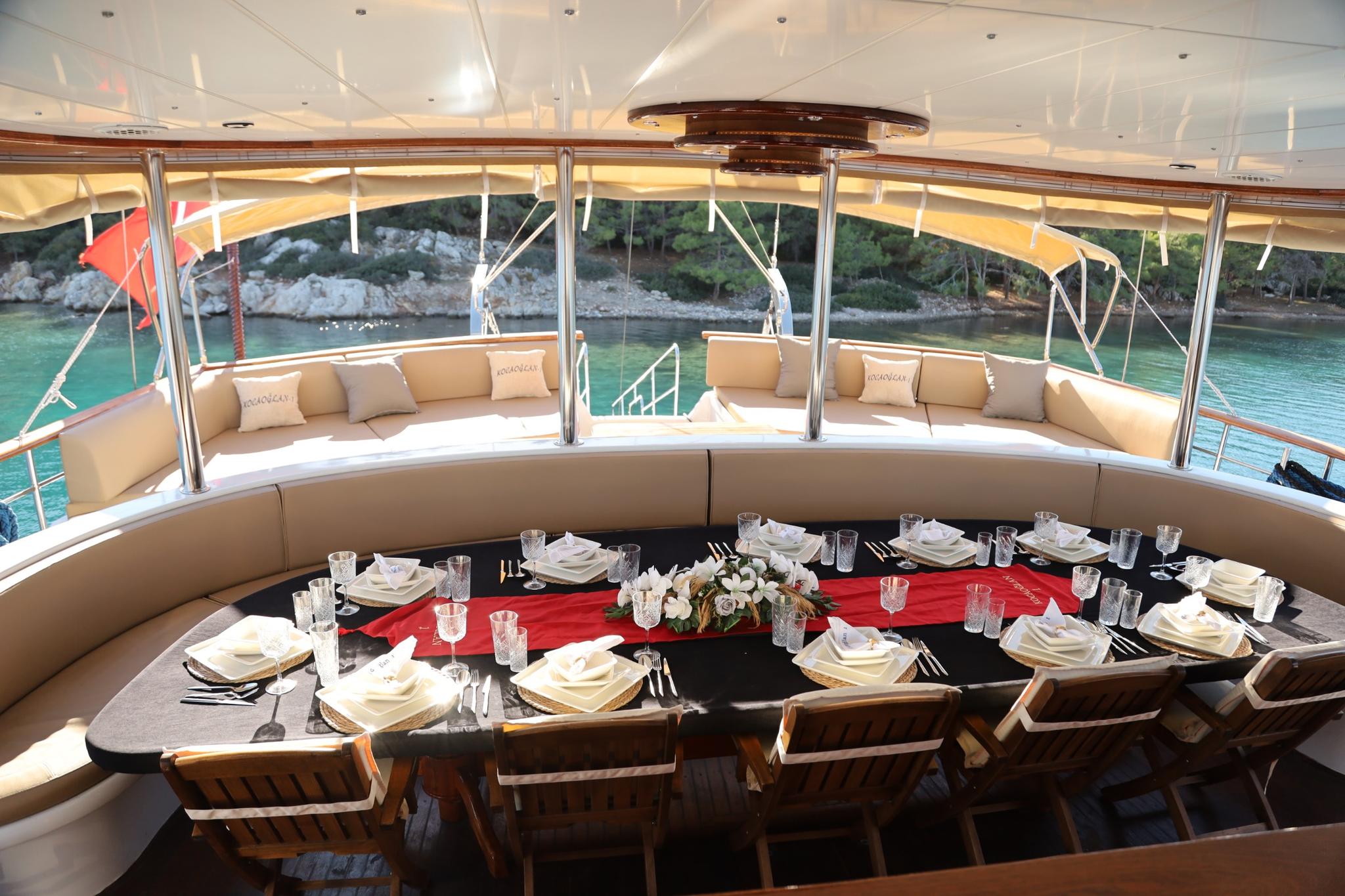 Curved aft deck dining area with formal table setting and cushioned seating overlooking turquoise waters