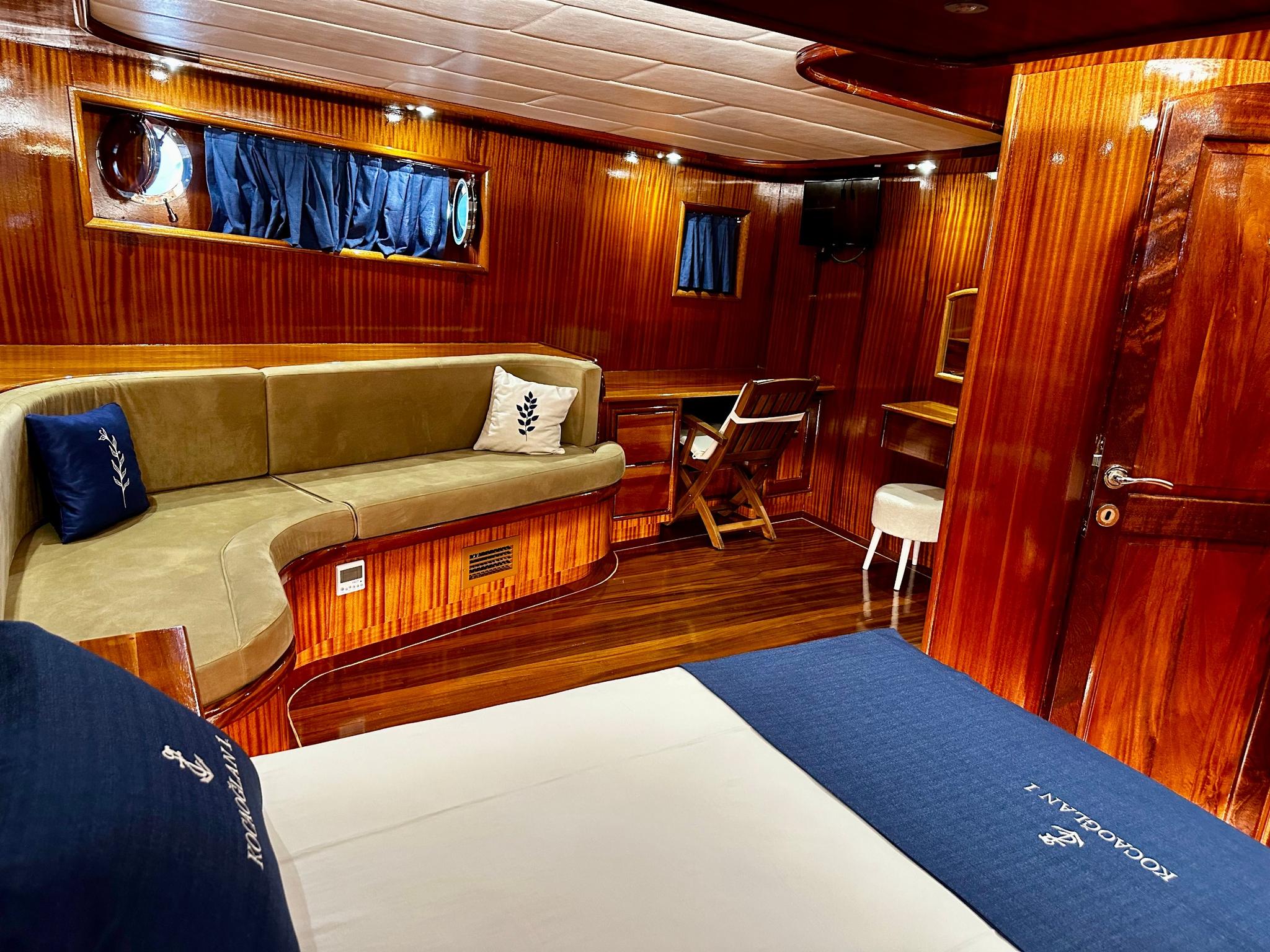 yacht guest cabin interior with double bed, curved seating banquette, mahogany paneling and portholes