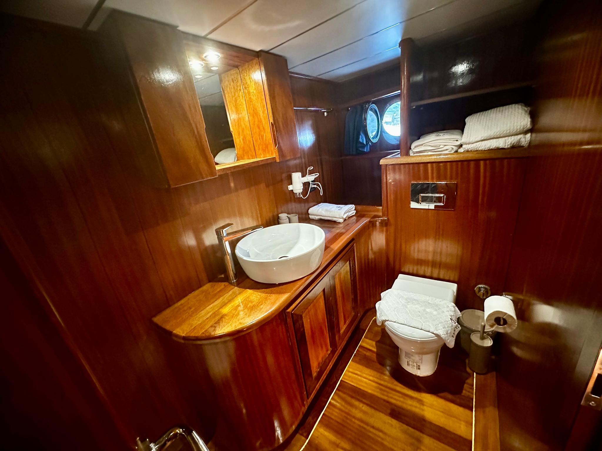 yacht bathroom with round white vessel sink on wooden vanity and toilet with towels