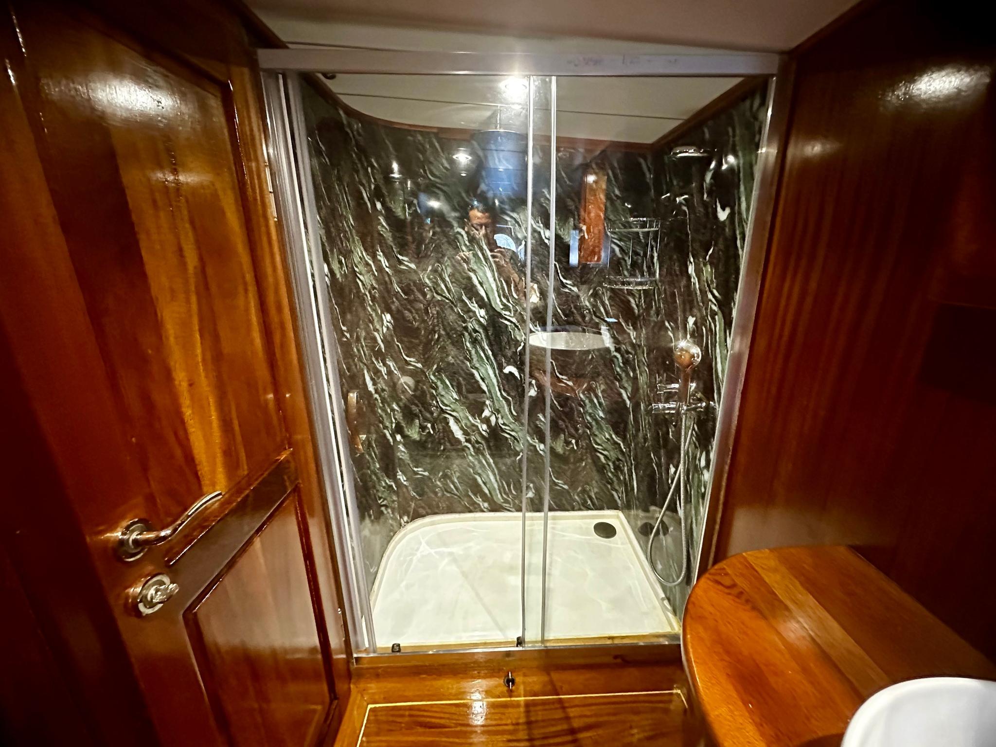 yacht bathroom featuring glass-enclosed shower with dark marble walls and white shower tray