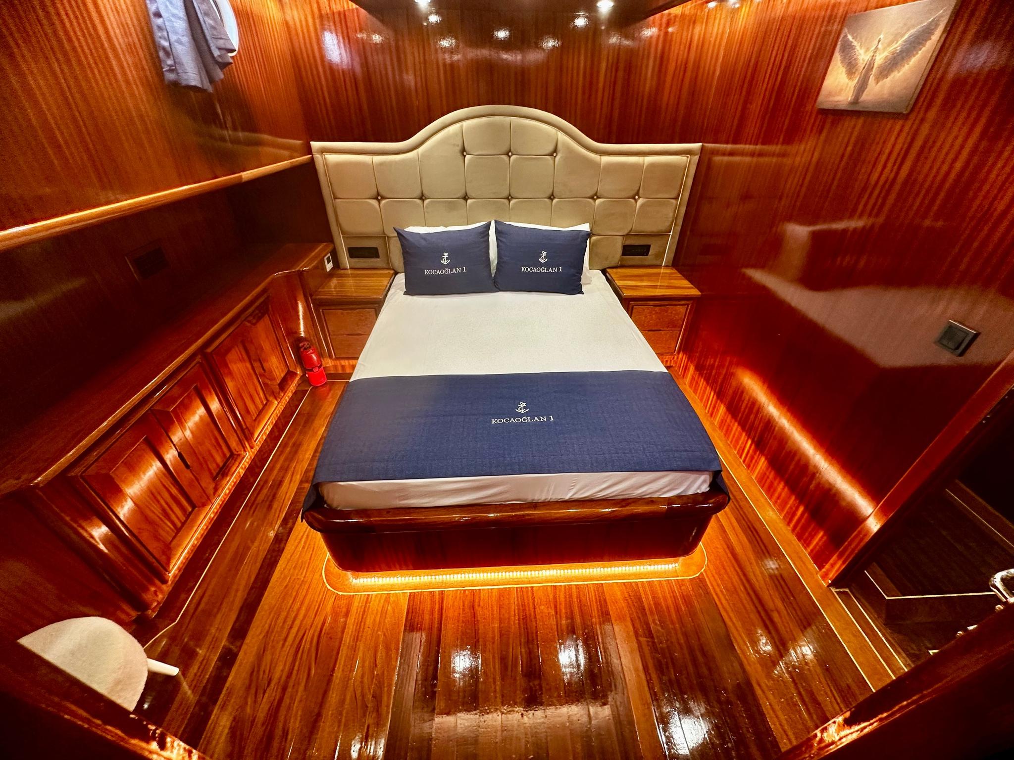 elegant yacht guest cabin featuring cream tufted headboard, navy branded pillows and runner, rich wood paneling