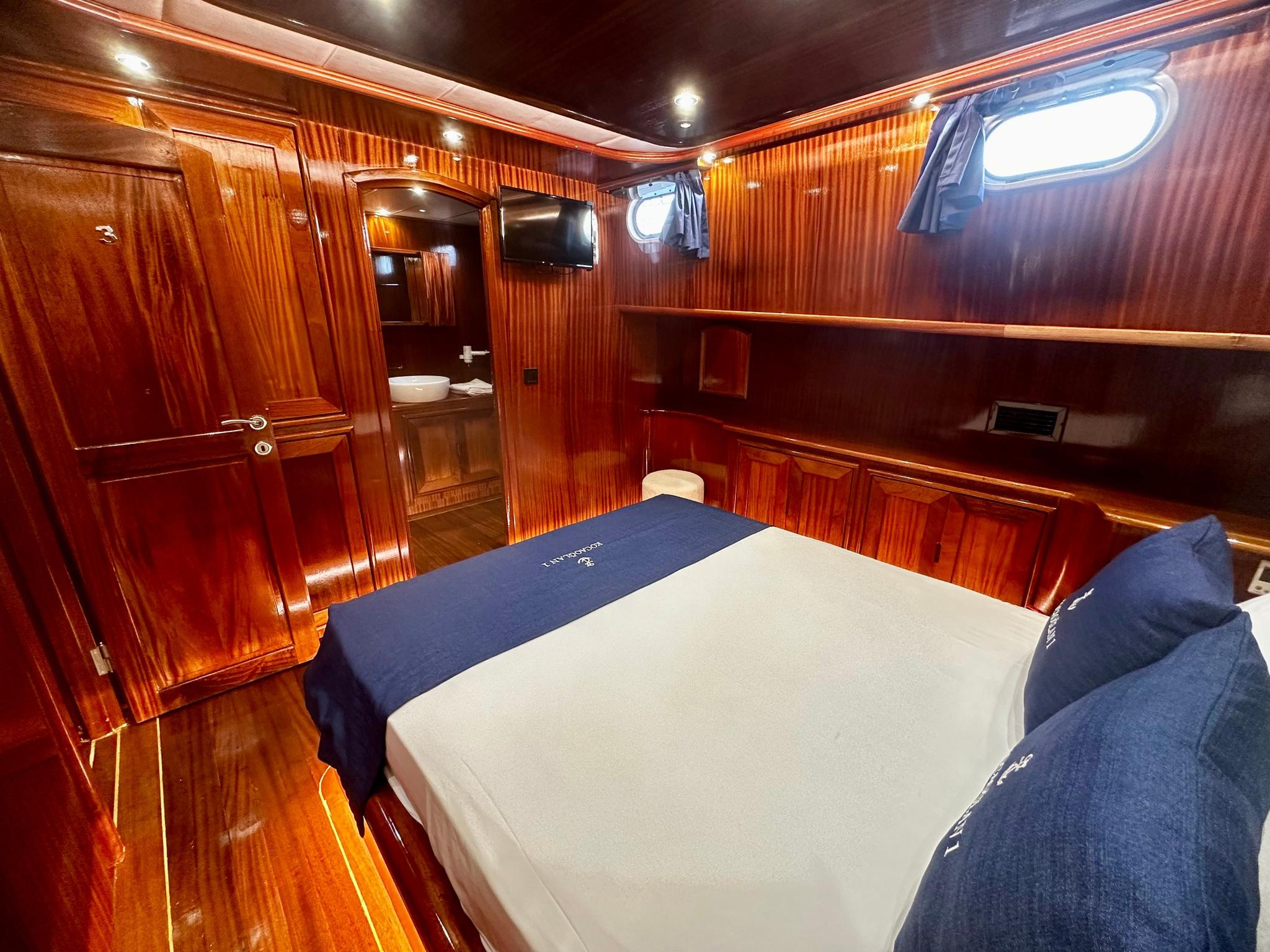 yacht guest cabin featuring double bed with navy bedding and rich wood paneled walls