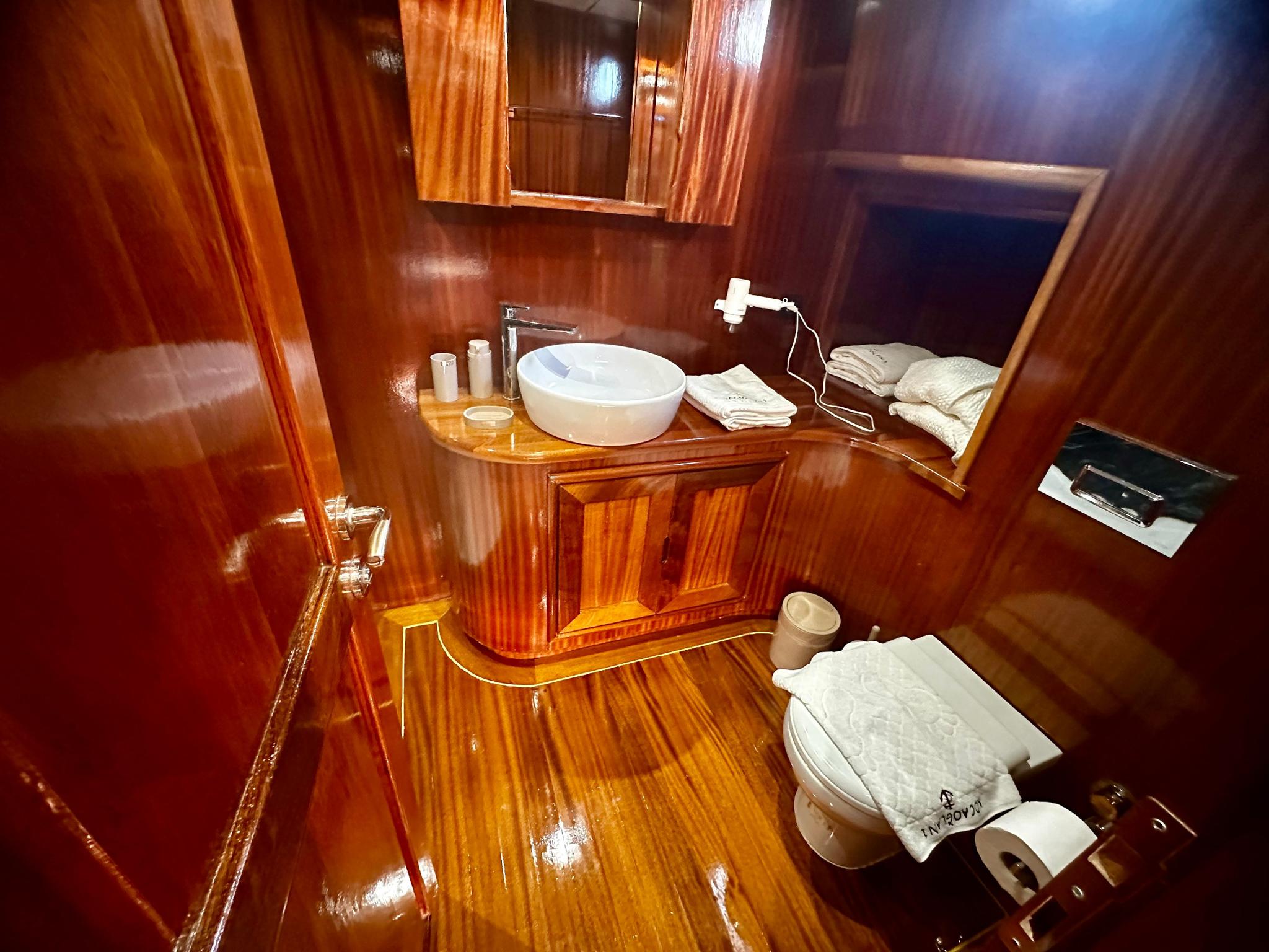 yacht bathroom featuring polished wood vanity with white basin and toilet