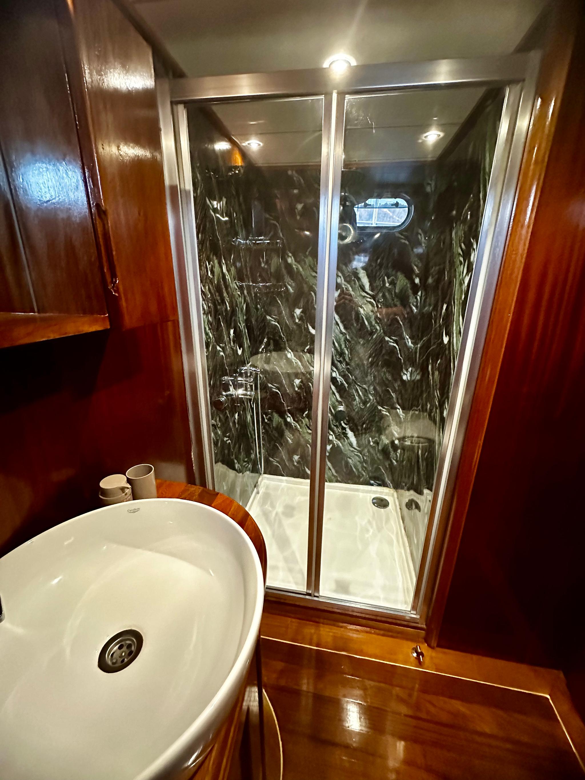 yacht bathroom featuring glass shower enclosure with marble walls and white ceramic sink