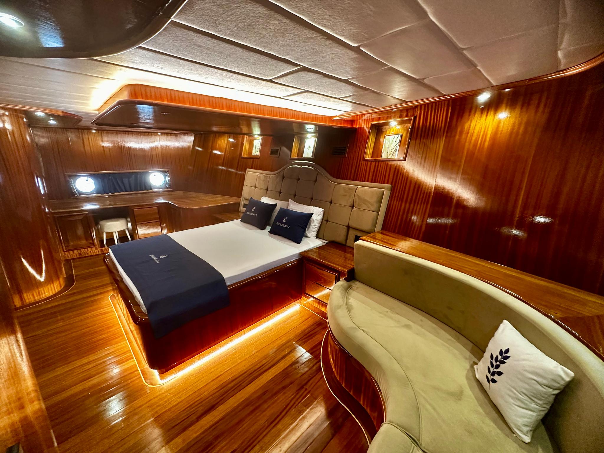 Master cabin interior with beige tufted headboard, white bedding, curved seating area and polished wood finishes