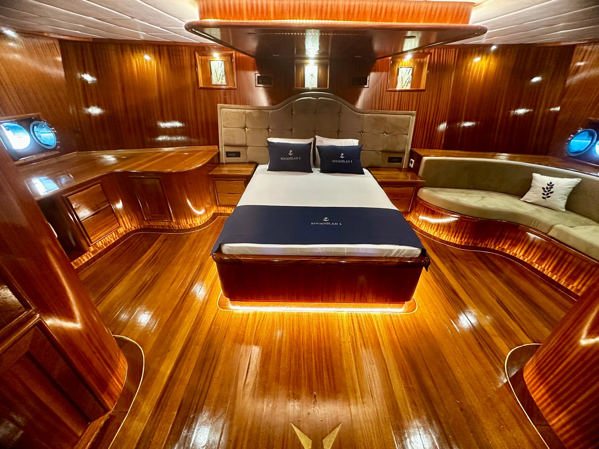 Master cabin interior with king bed, beige upholstered headboard, mahogany paneling and portholes