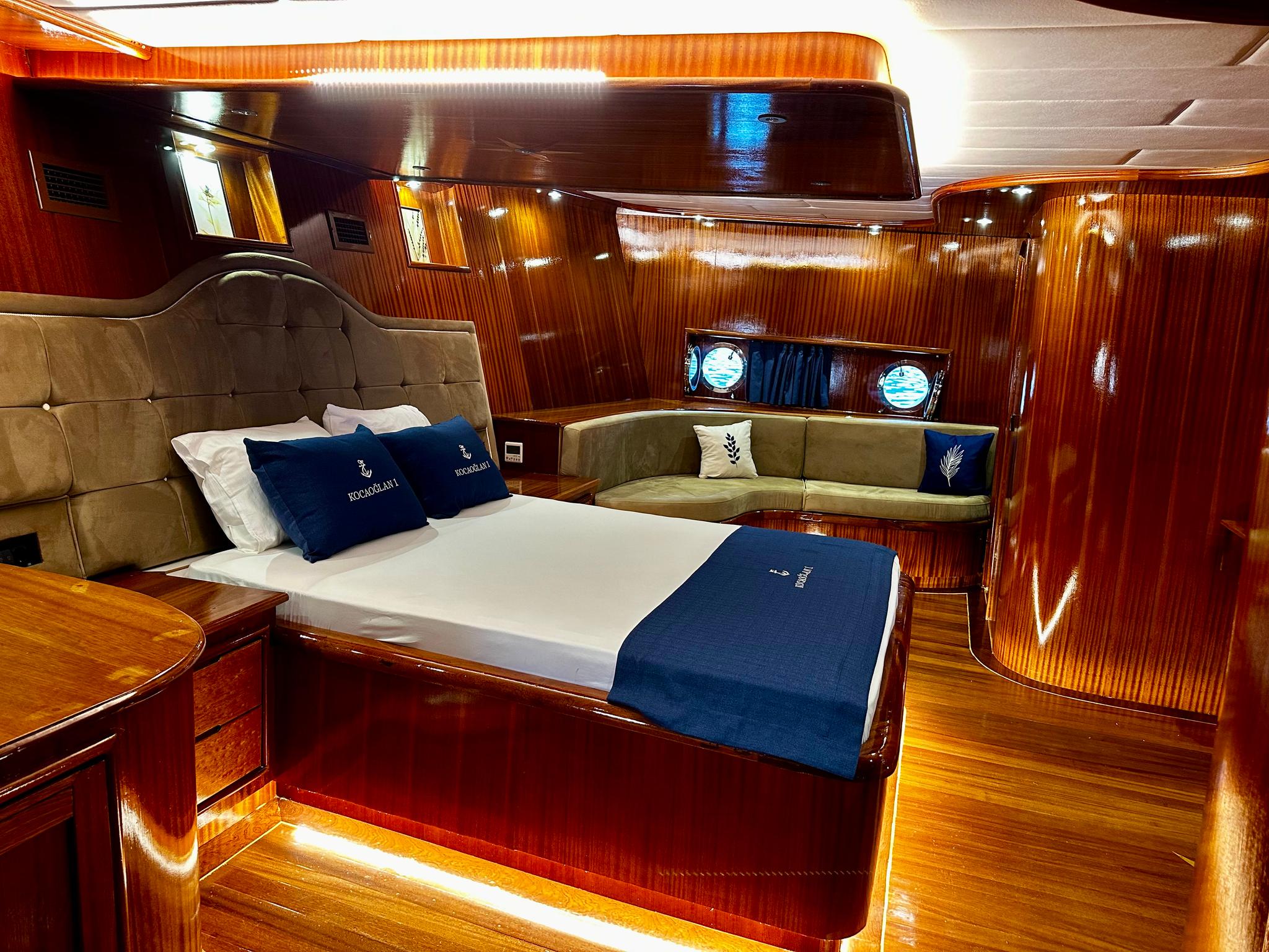 Master cabin interior with double bed, tufted headboard, seating area and portholes