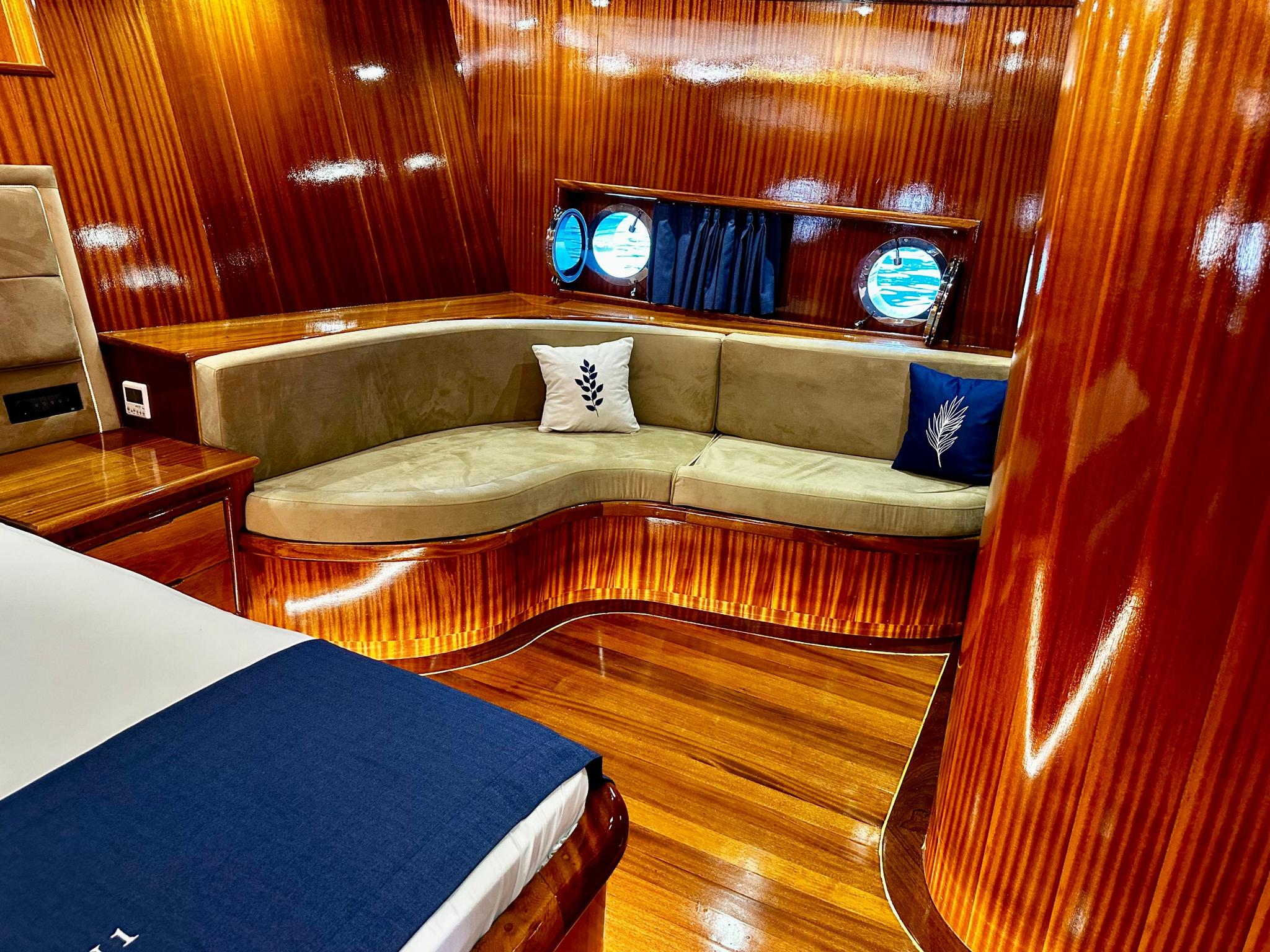 yacht cabin with beige curved banquette seating, decorative pillows and three round portholes