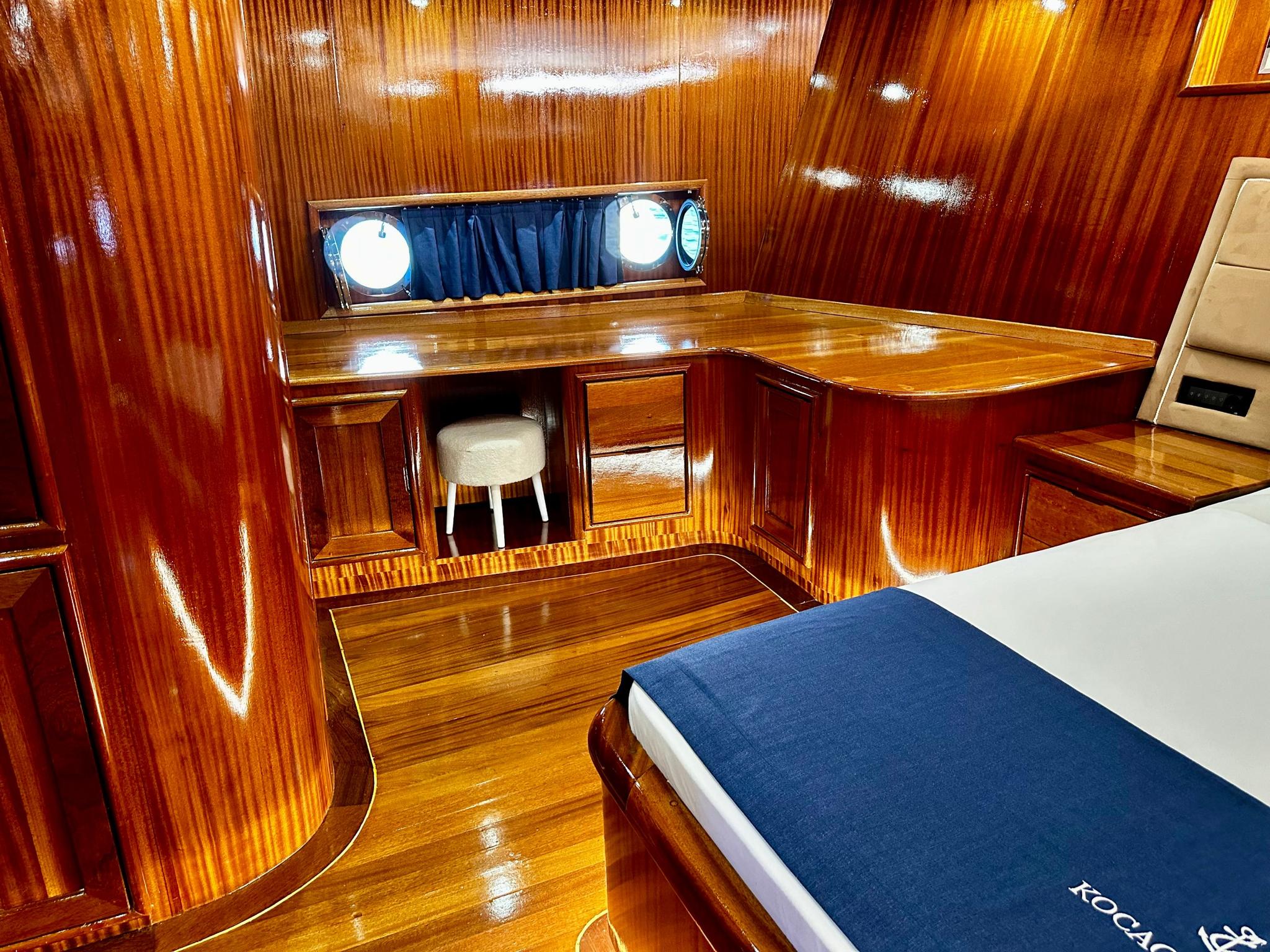 yacht cabin with single bed, built-in wooden desk, portholes and cream upholstery