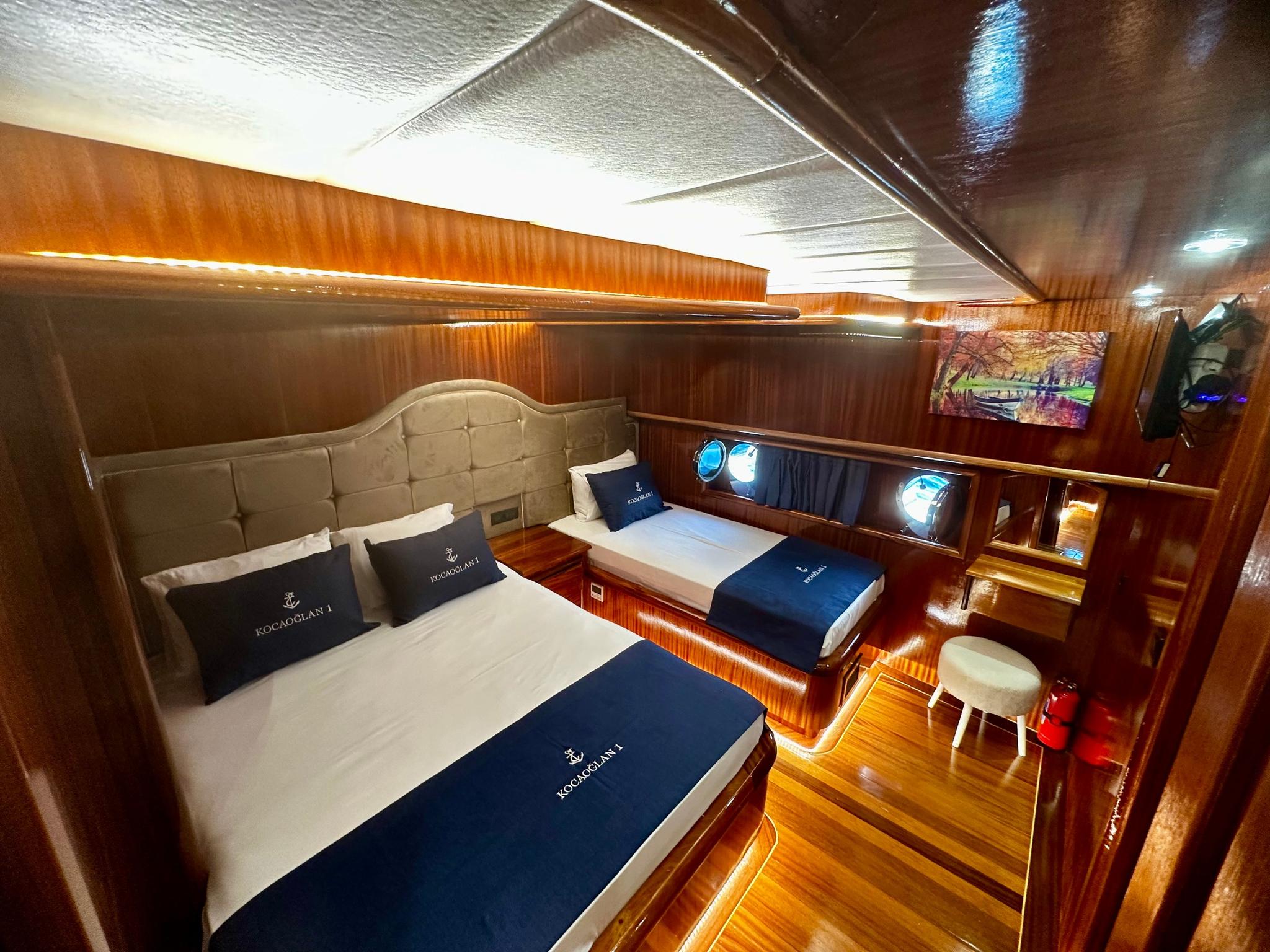 luxury yacht twin cabin with beige tufted headboard, white bedding, navy blue runners and round portholes