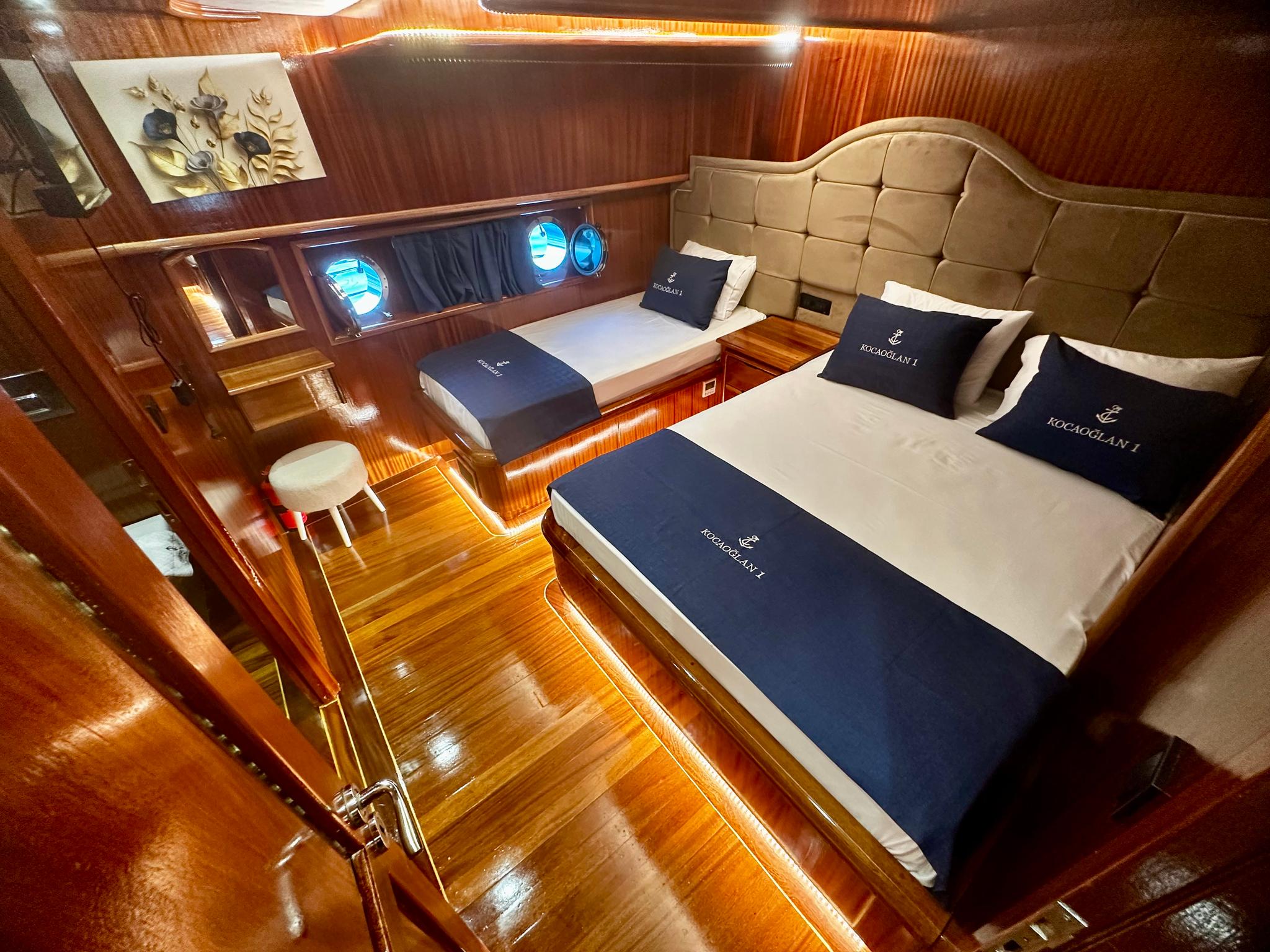 guest cabin featuring two single beds with navy blue bedding, cream leather headboards, and circular portholes