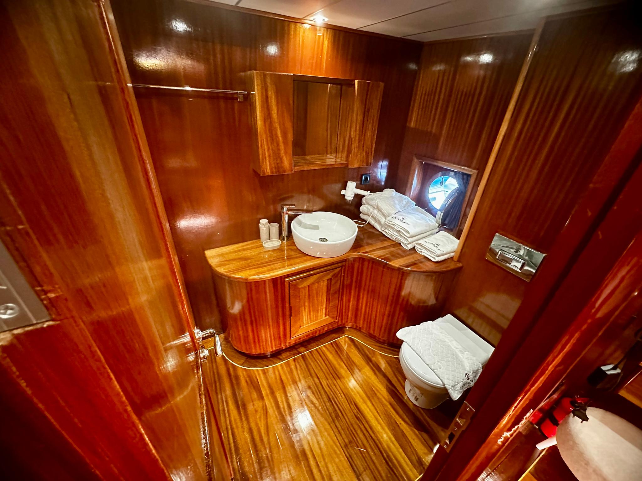 luxury yacht ensuite bathroom featuring white basin, toilet, and polished wood cabinetry