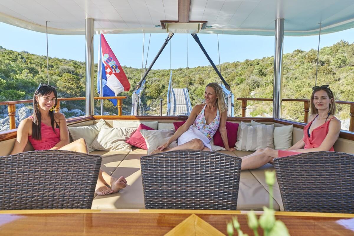 Three female guests relaxing on yacht aft deck wicker seating with Croatian flag