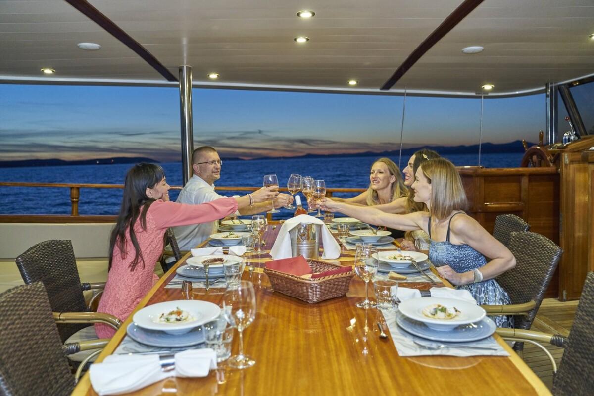 Five guests raising wine glasses in toast at elegant yacht dining table during sunset