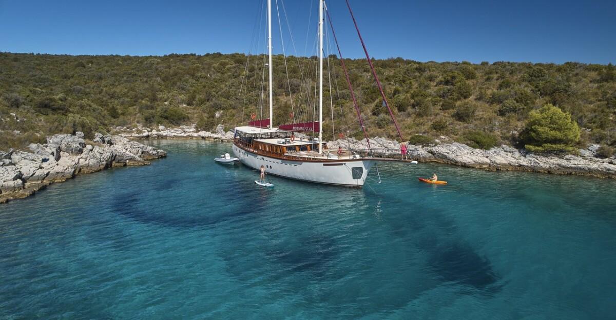 Traditional wooden gulet yacht anchored in crystal clear turquoise bay with rocky coastline