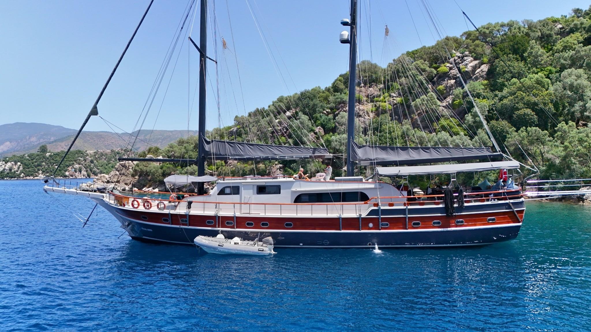 traditional wooden gulet yacht with two masts anchored in crystal clear Mediterranean waters near forested coastline