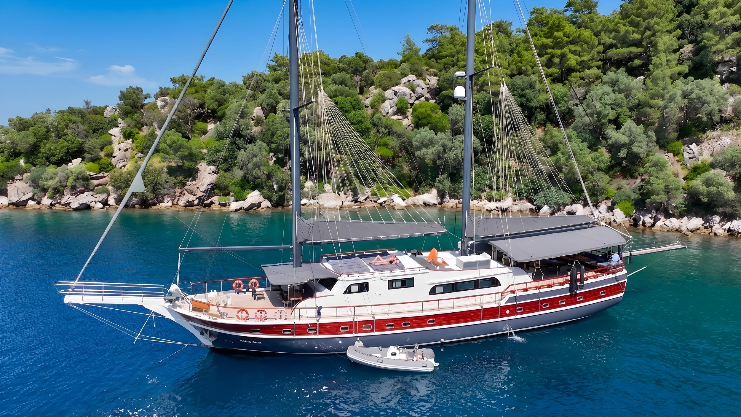 Traditional wooden gulet yacht with red hull anchored in crystal clear turquoise waters near forested coastline