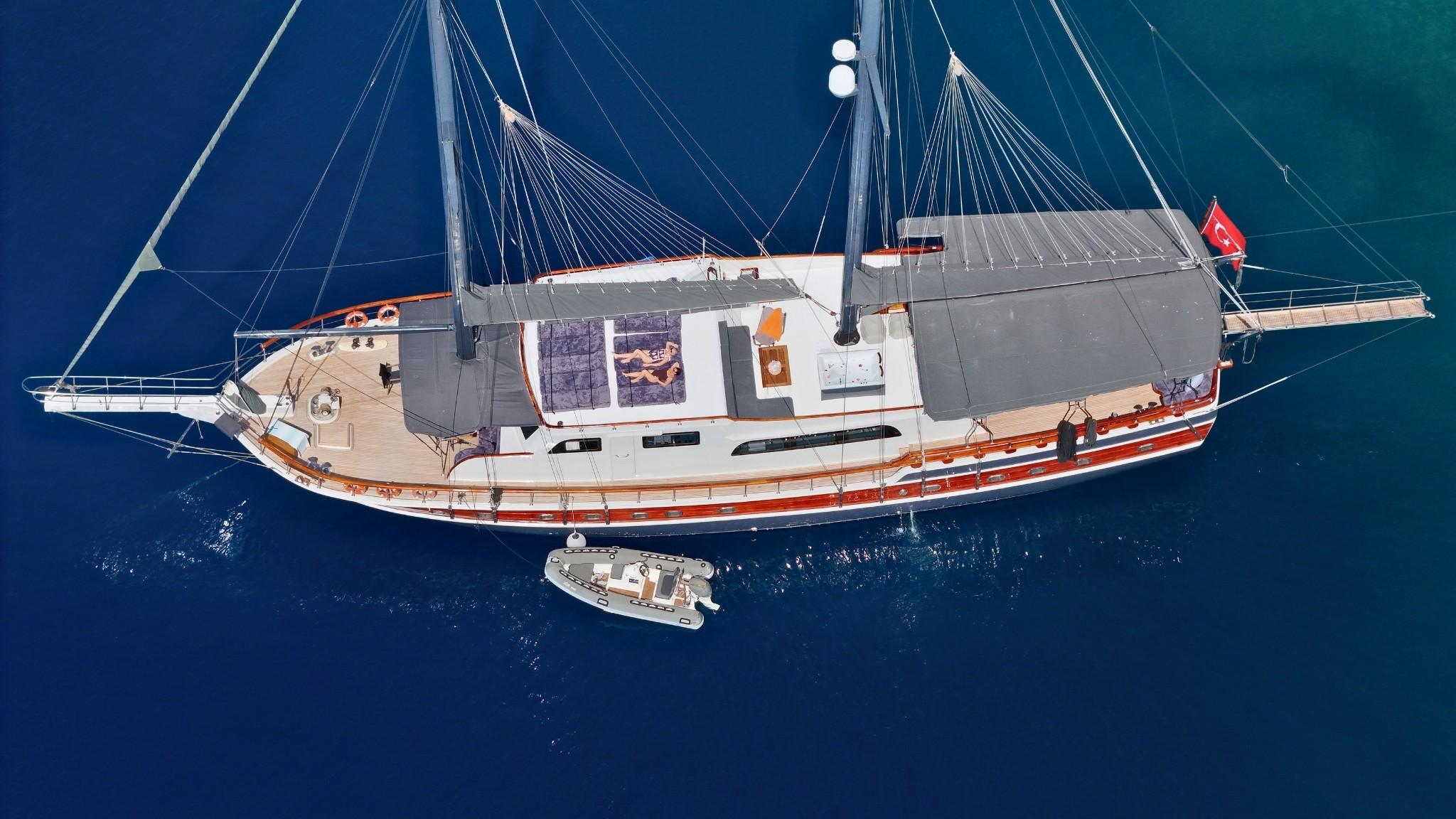 aerial view of traditional wooden gulet yacht anchored in deep blue waters with small tender boat alongside