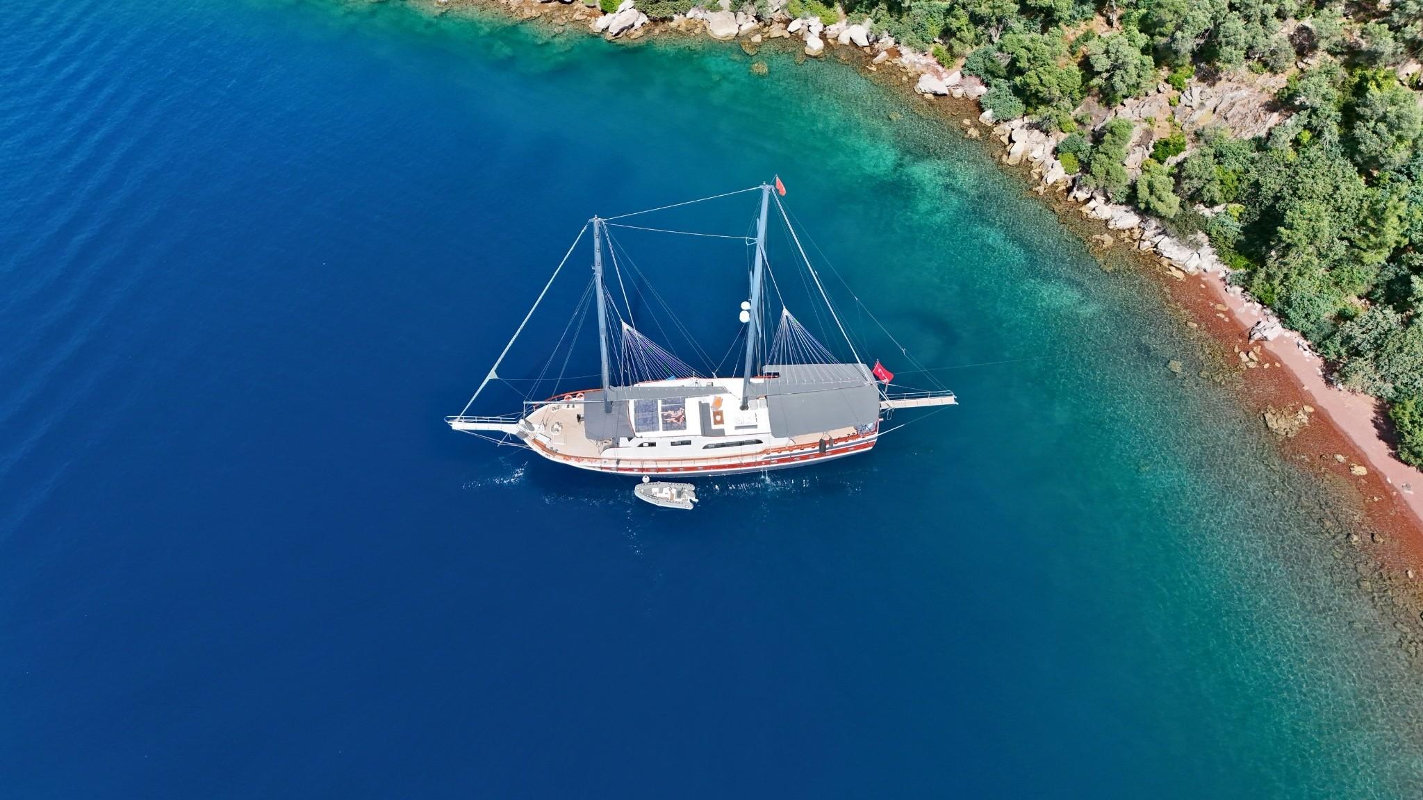 aerial view of white traditional gulet yacht anchored in turquoise Mediterranean bay near forested coastline