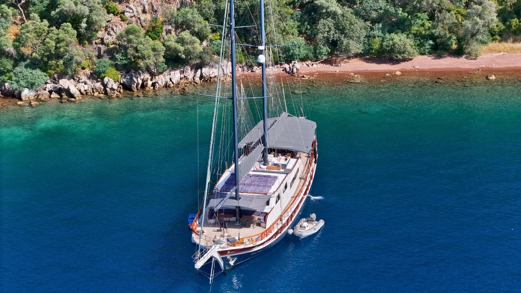 aerial view of traditional wooden gulet yacht anchored in crystal clear turquoise waters near Mediterranean coastline