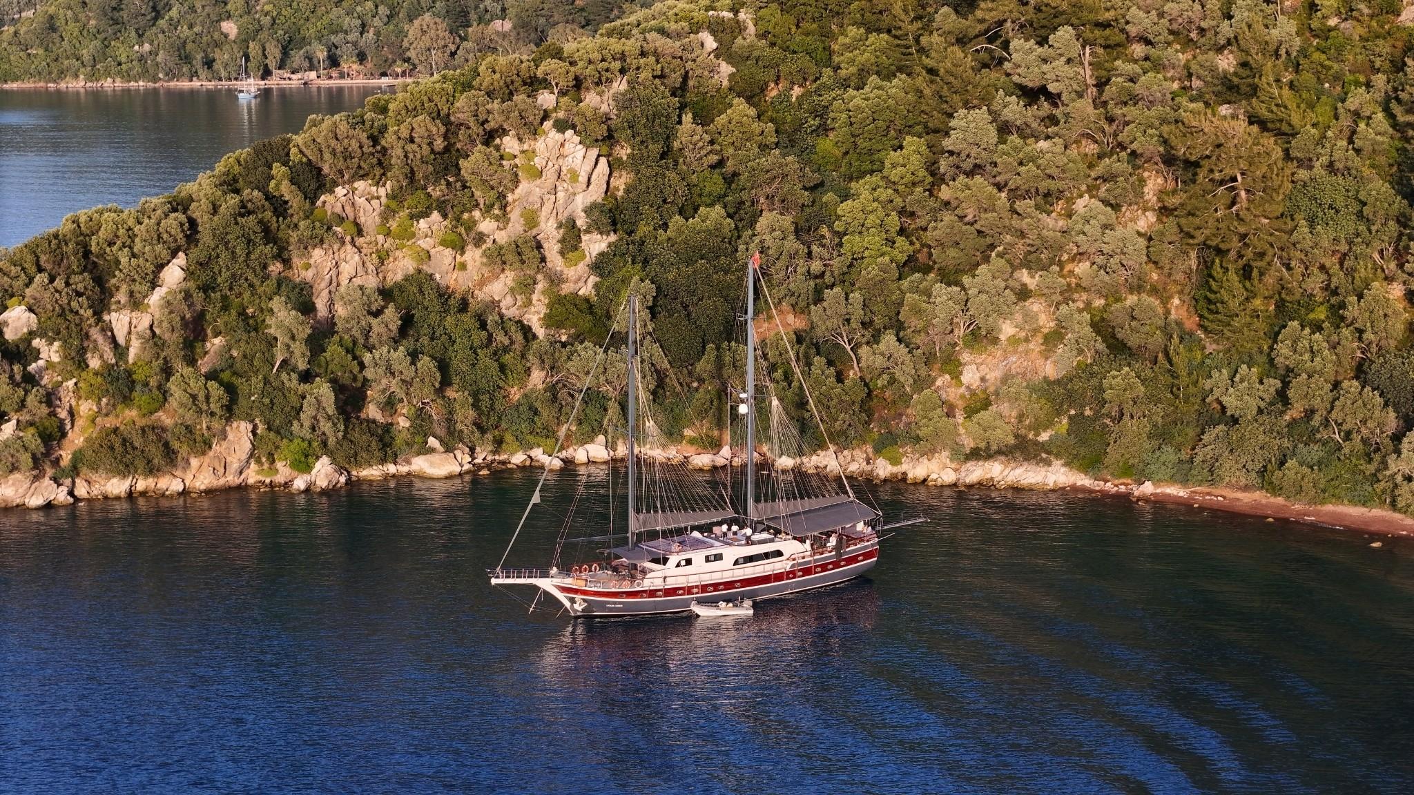 aerial view of traditional gulet yacht anchored in pristine cove with rocky coastline