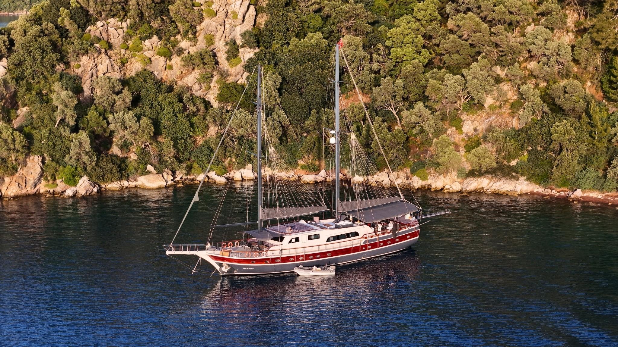 Traditional wooden gulet yacht with two masts anchored in Mediterranean bay near rocky coastline