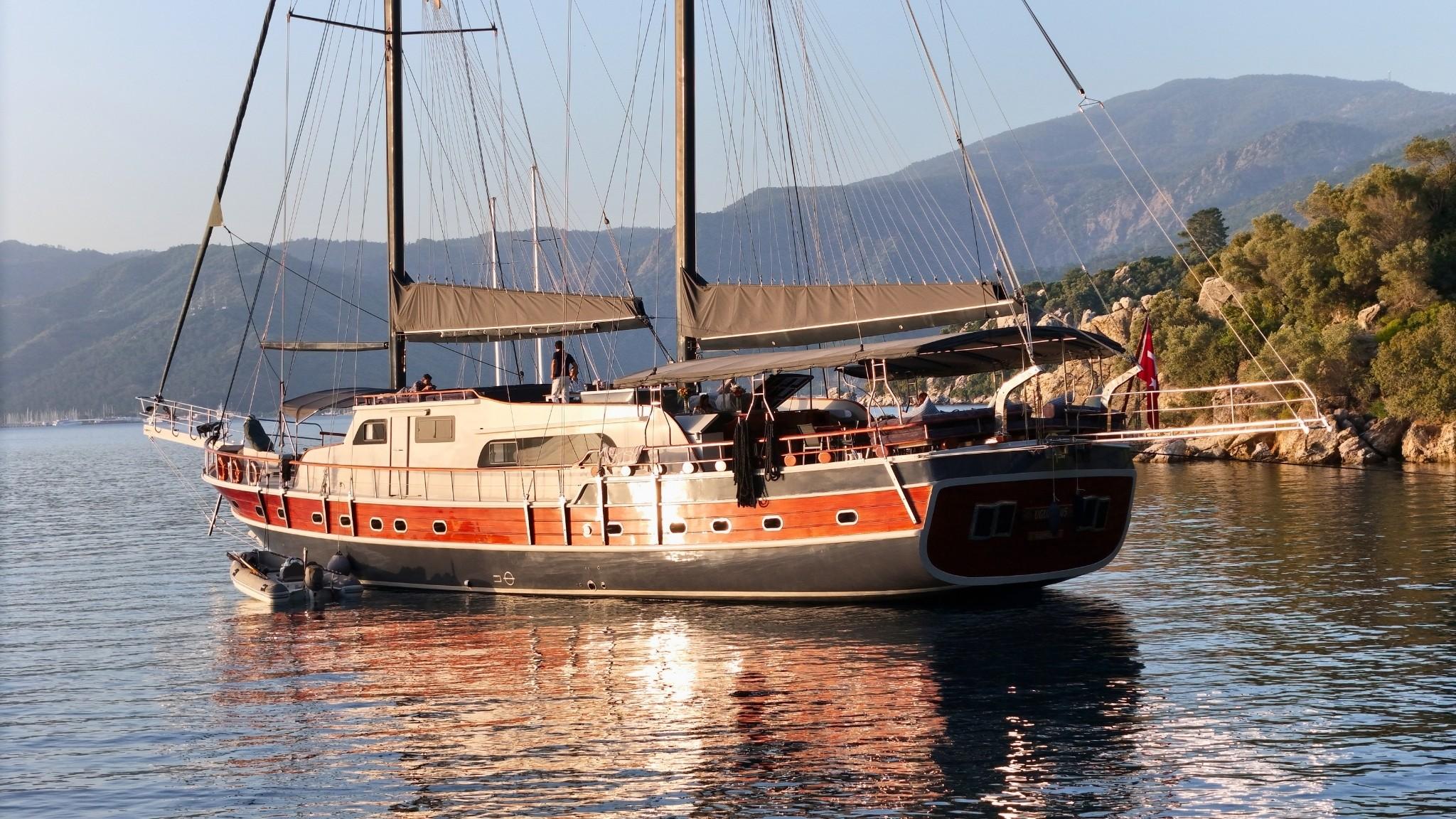 Traditional wooden gulet yacht with two masts anchored in calm Mediterranean waters near rocky coastline