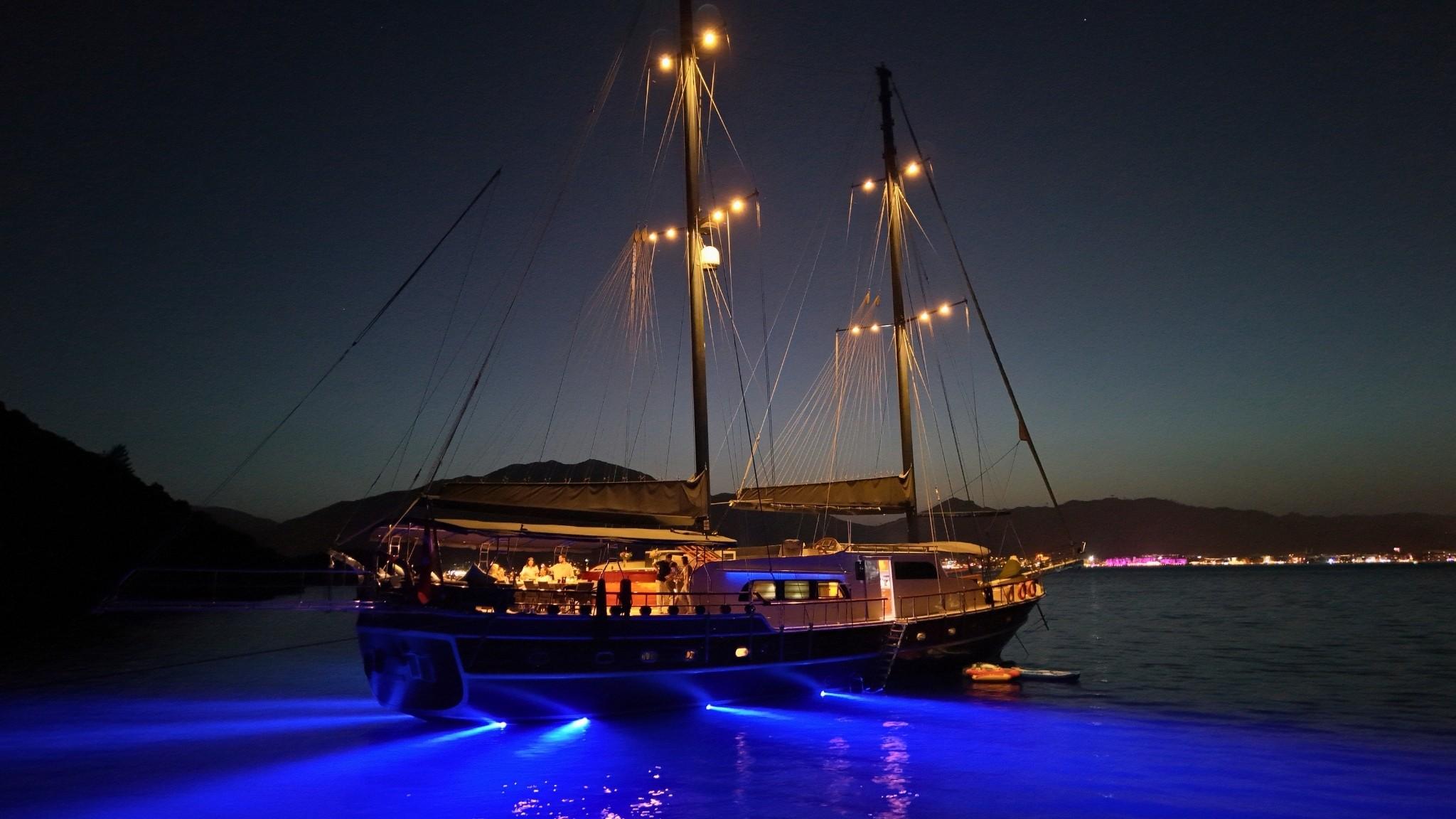luxury gulet yacht with blue underwater LED lighting illuminating water at twilight anchorage