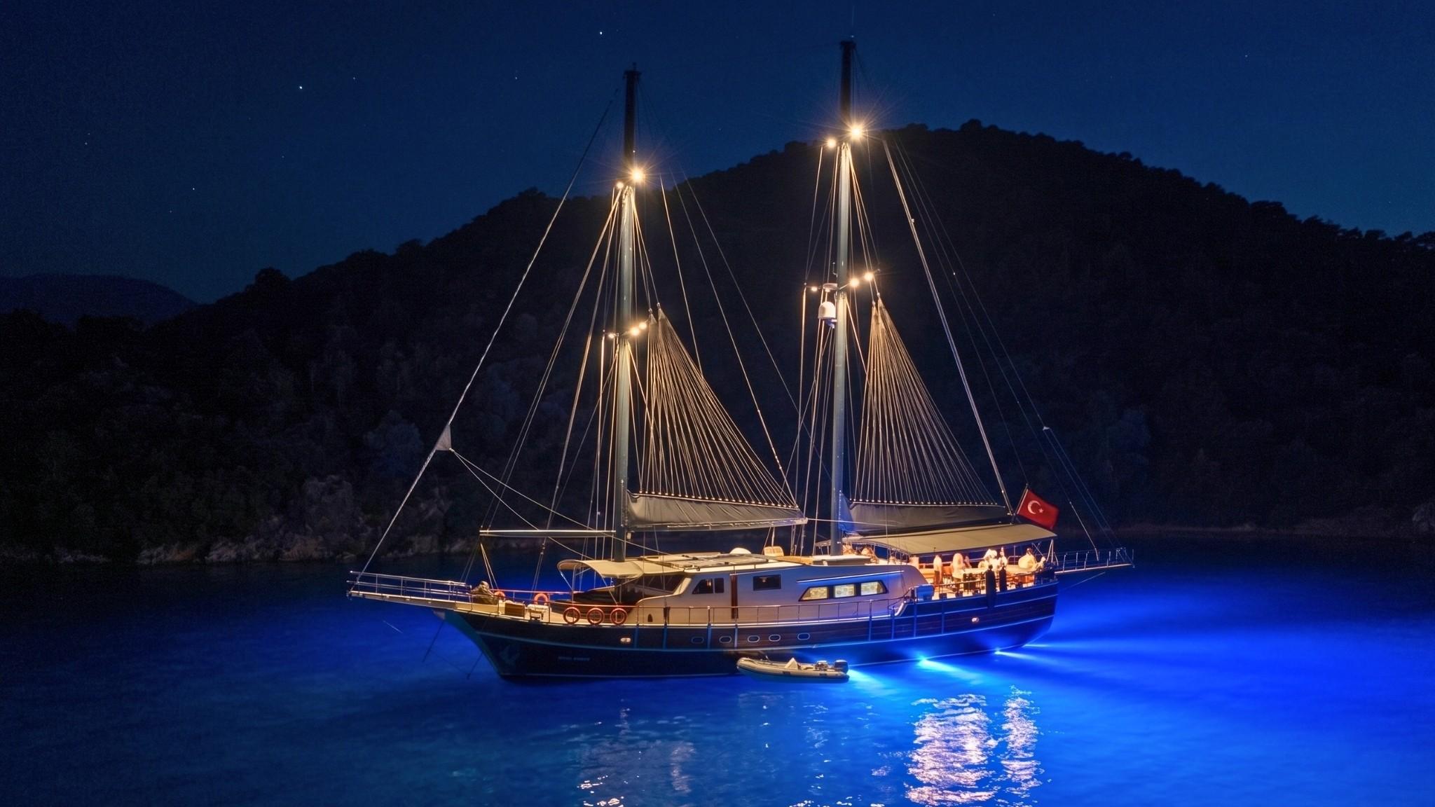 Traditional wooden gulet yacht anchored in calm waters at night with blue underwater lighting and Turkish flag