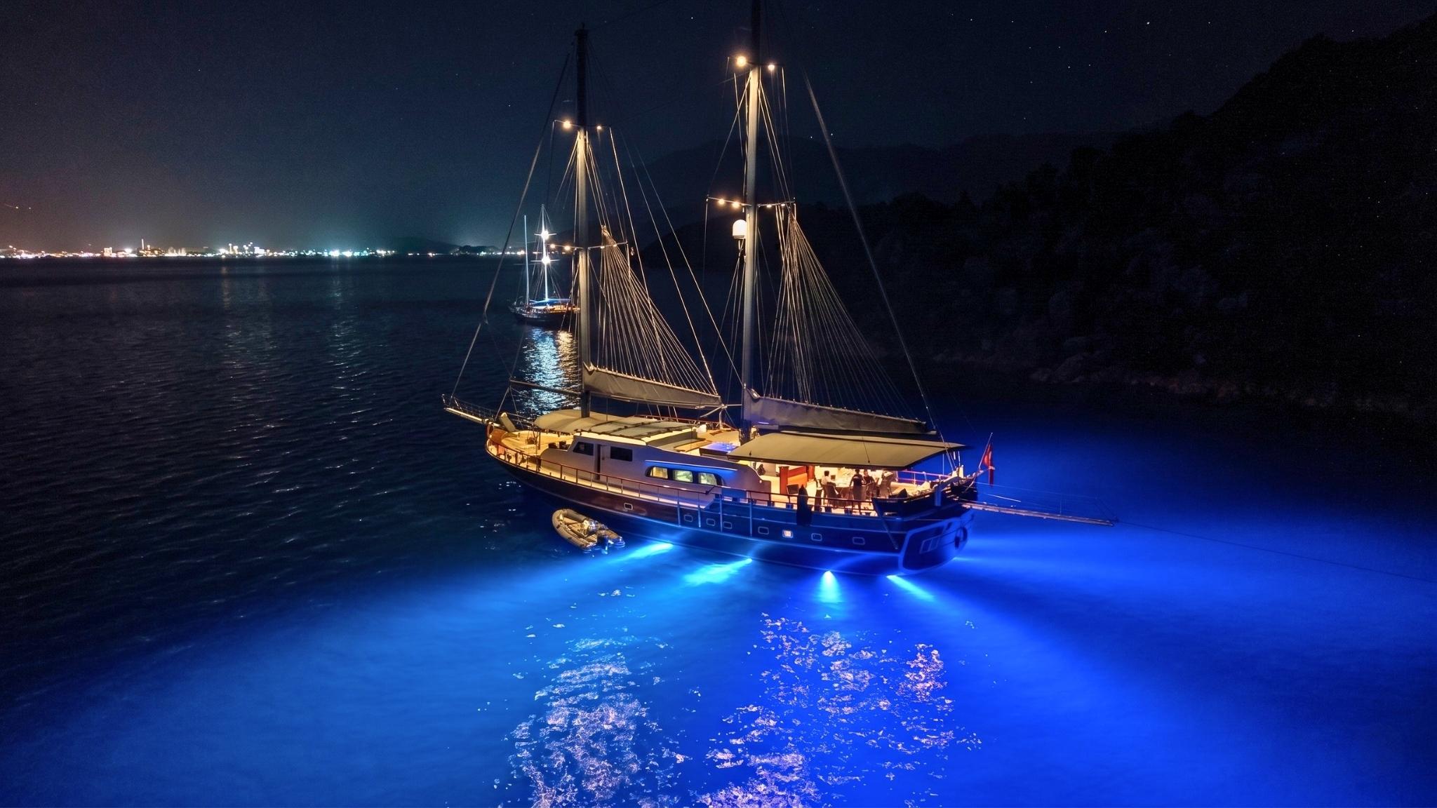 traditional gulet yacht with blue underwater LED lights illuminating water at night anchorage