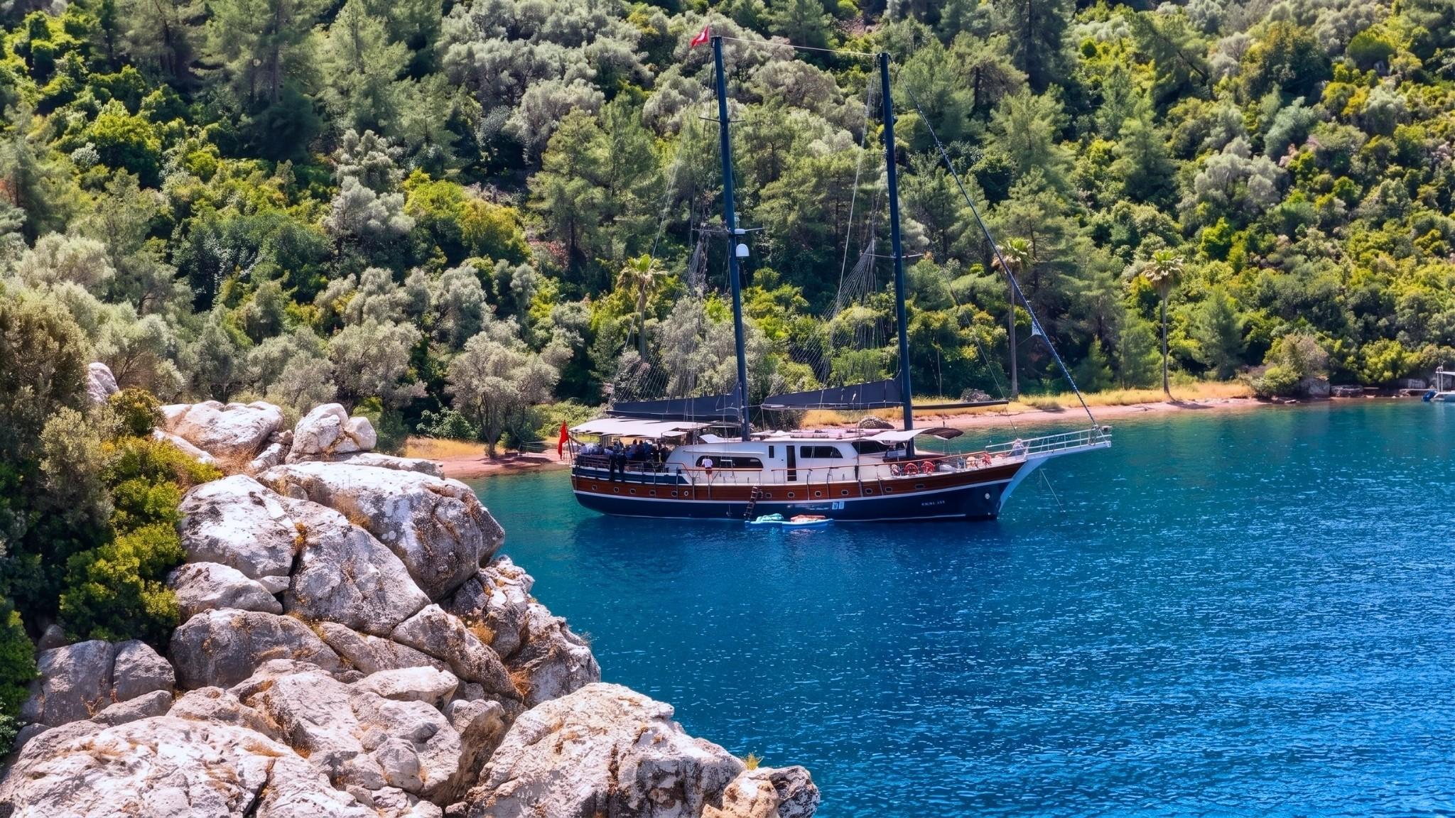 Traditional wooden gulet yacht anchored in secluded turquoise bay near forested coastline