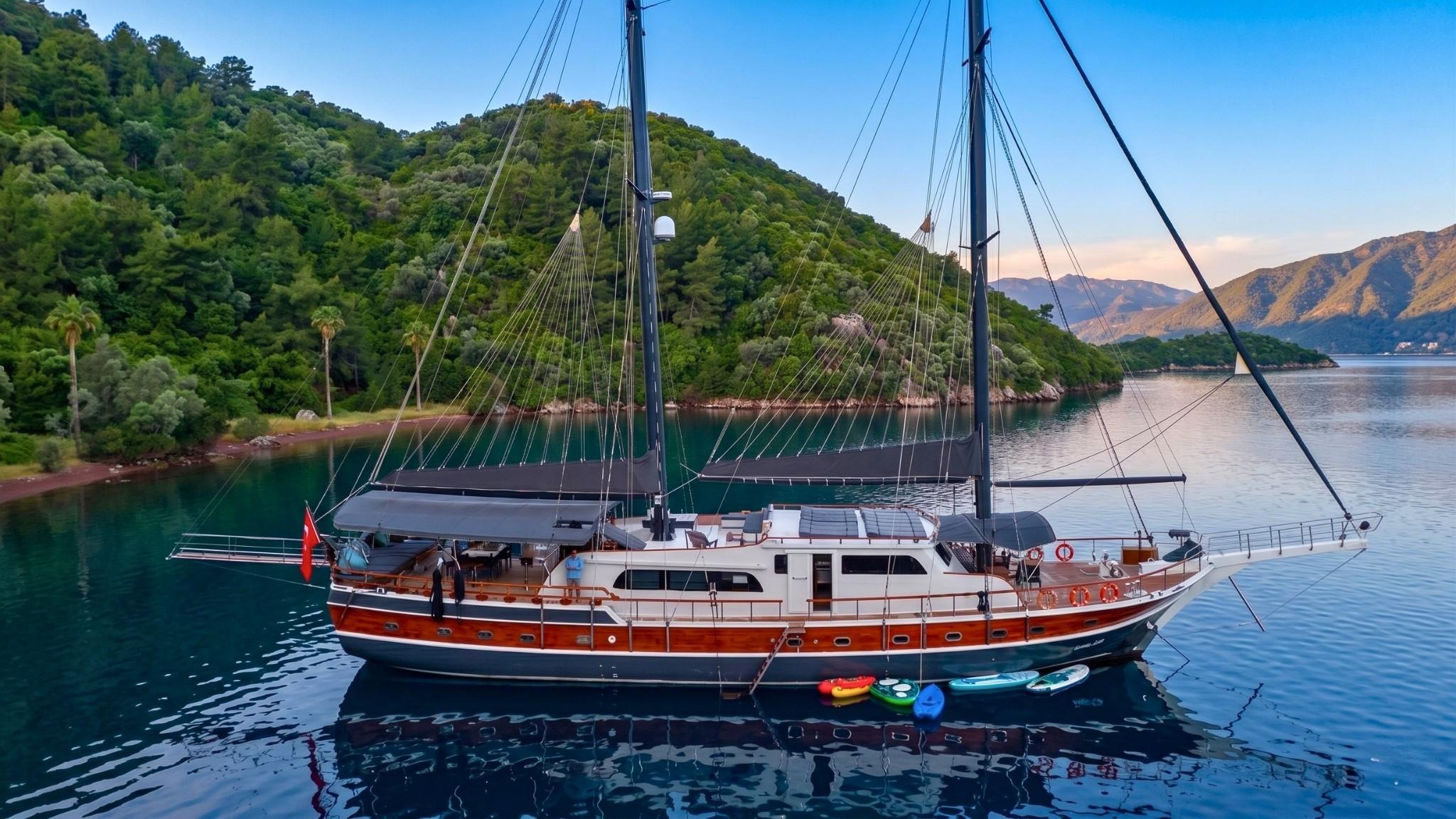 traditional wooden gulet yacht anchored in bay with colorful kayaks tied at stern