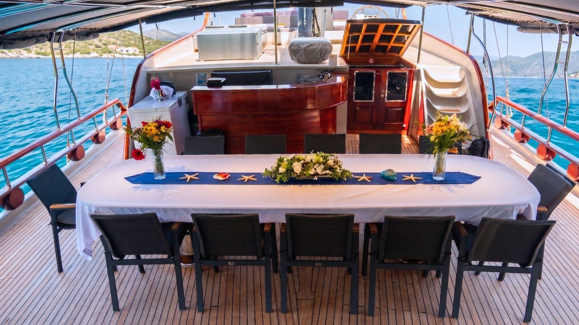 gulet aft deck with formal dining table, white tablecloth, floral centerpiece and dark chairs