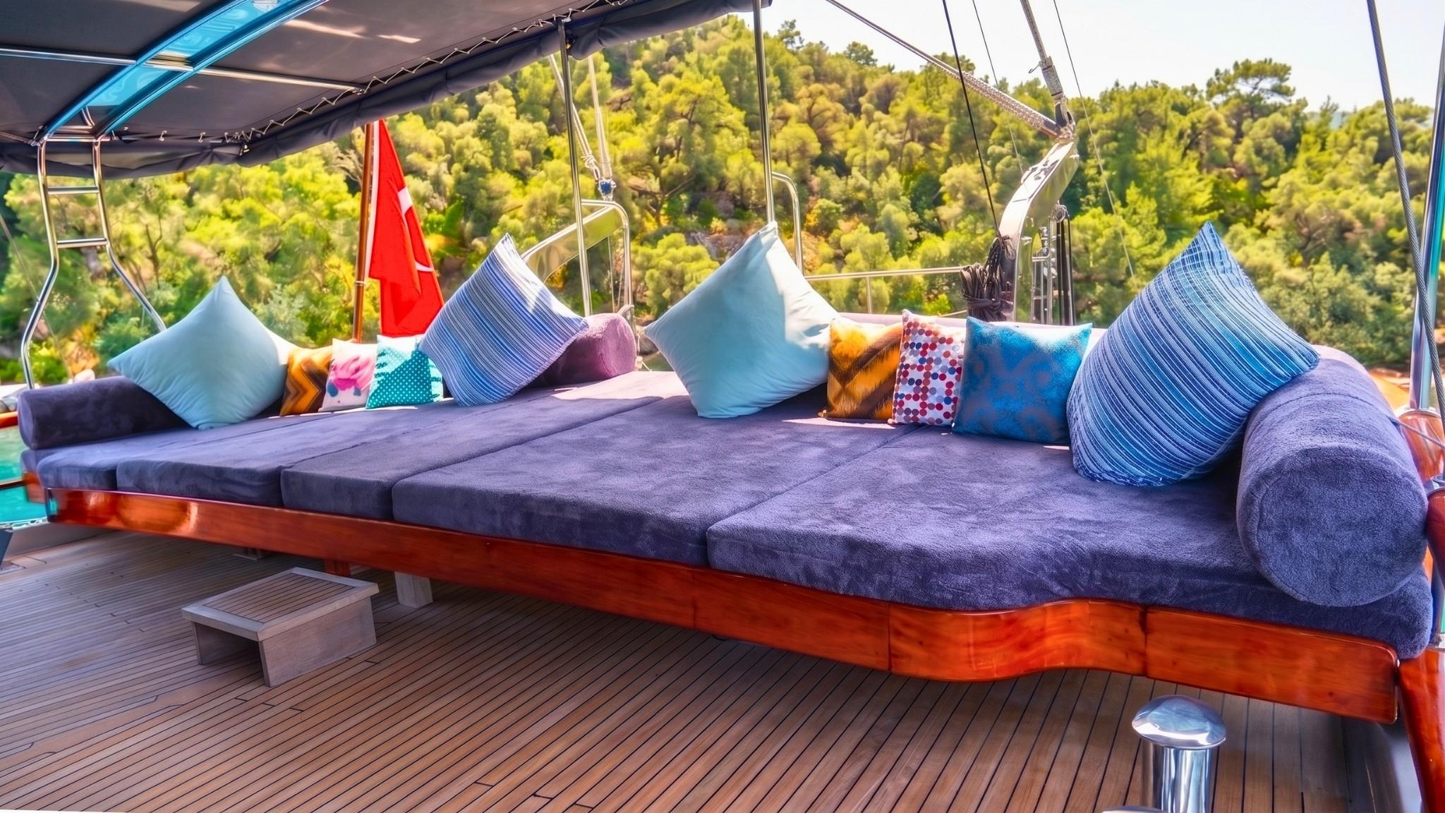 Yacht deck lounge area with blue cushioned daybed and colorful pillows under awning
