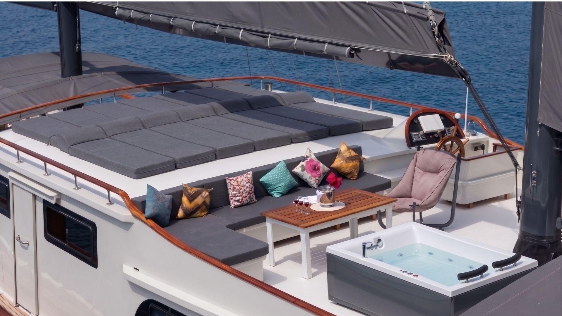 yacht upper deck featuring white jacuzzi, grey sectional seating with colorful cushions, helm station