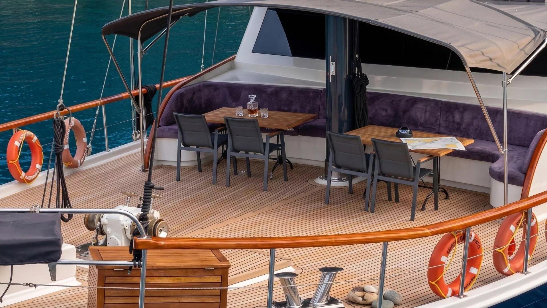 Yacht aft deck with purple cushioned seating, teak dining tables and black chairs
